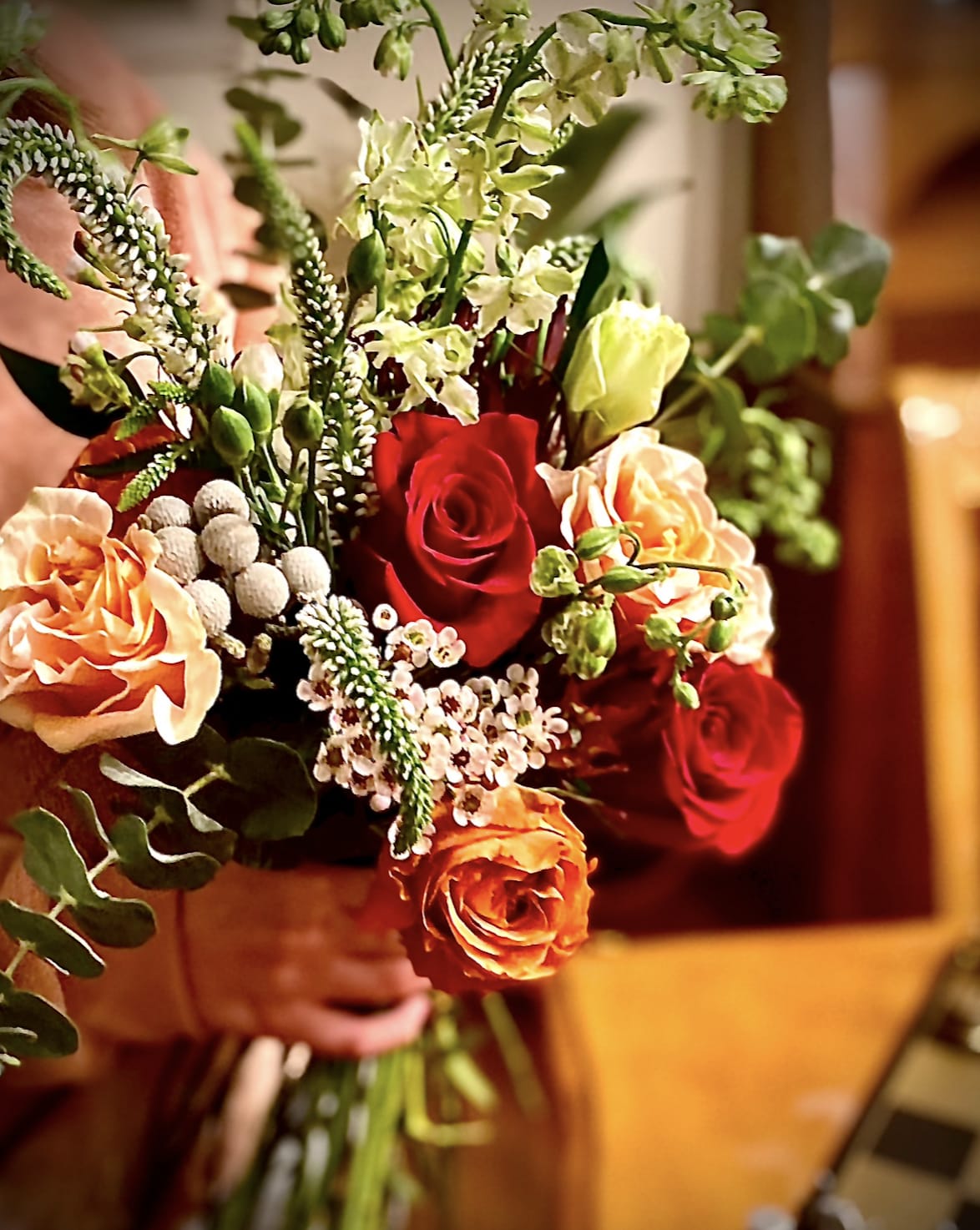 Hand-tied bouquet with red and orange roses, peach blooms, and small white accent flowers.