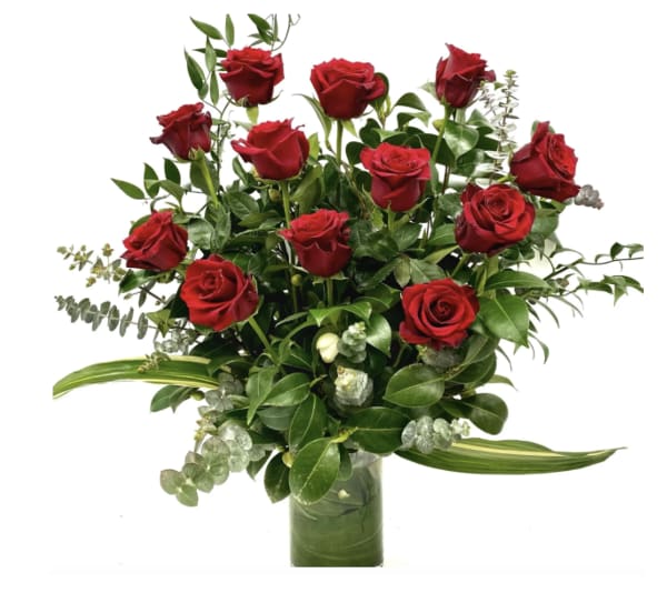 Arrangement of red roses with lush greenery in a clear cylinder vase