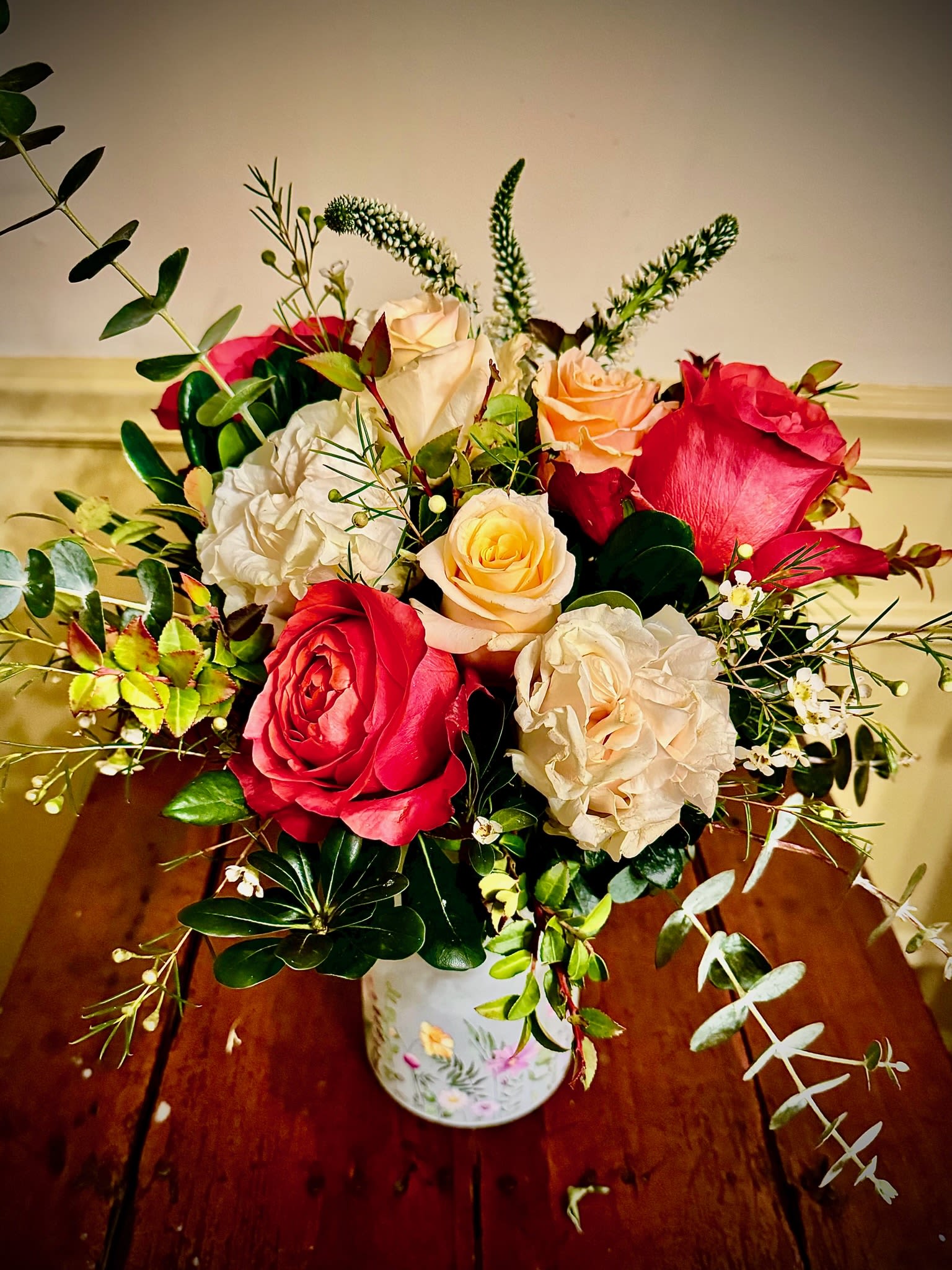Mixed red and cream roses with peach blooms and trailing eucalyptus in a painted white vase
