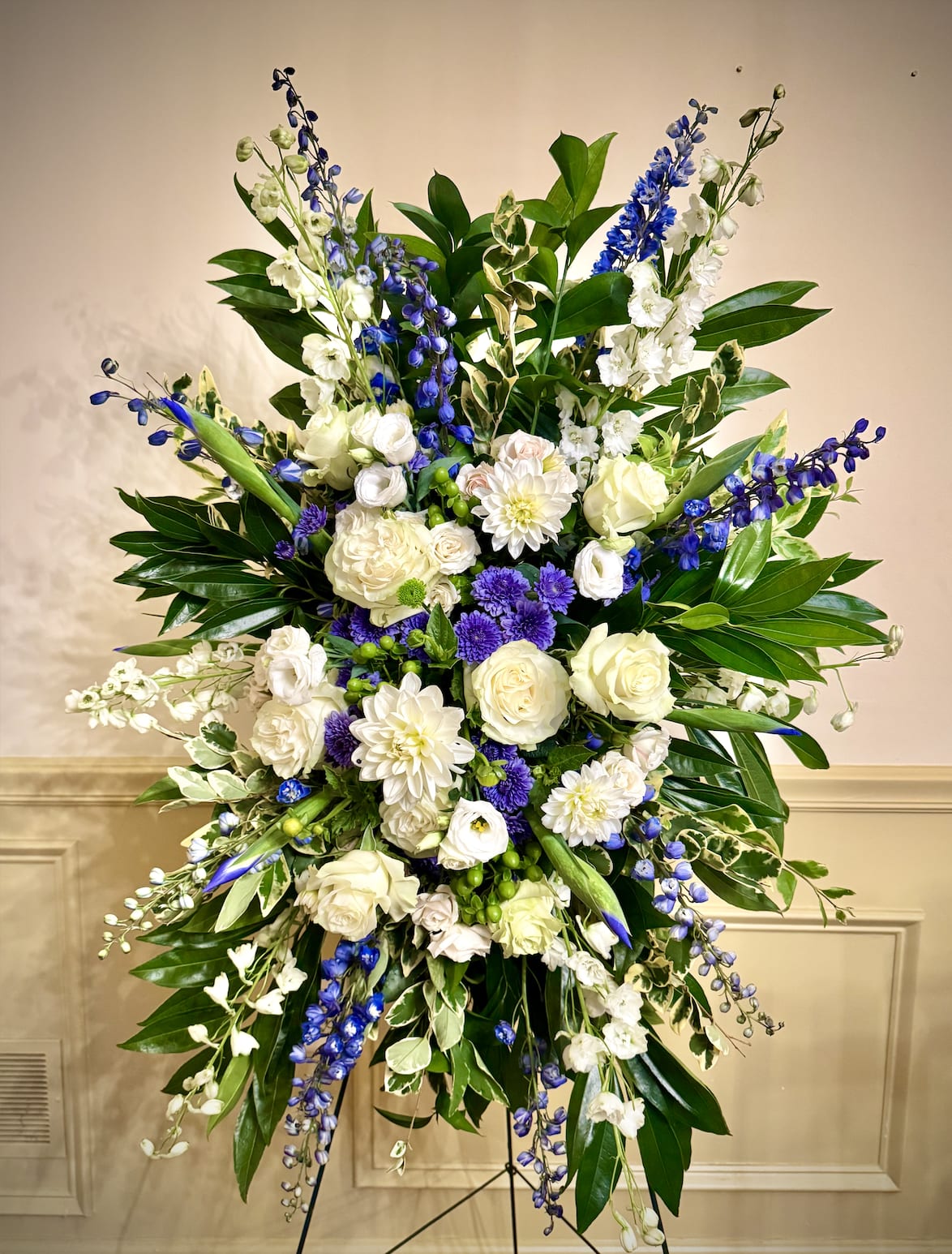 Tall standing spray of white and purple flowers with blue accents on a metal easel