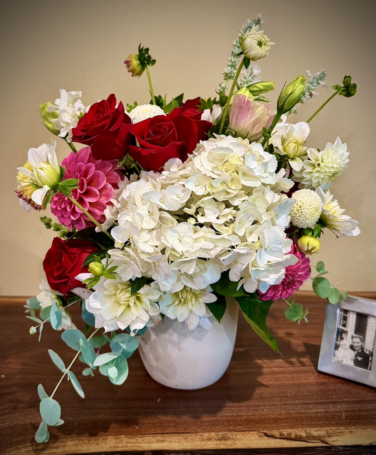 Mixed arrangement of red roses, white hydrangeas, and pink dahlias in a white vase
