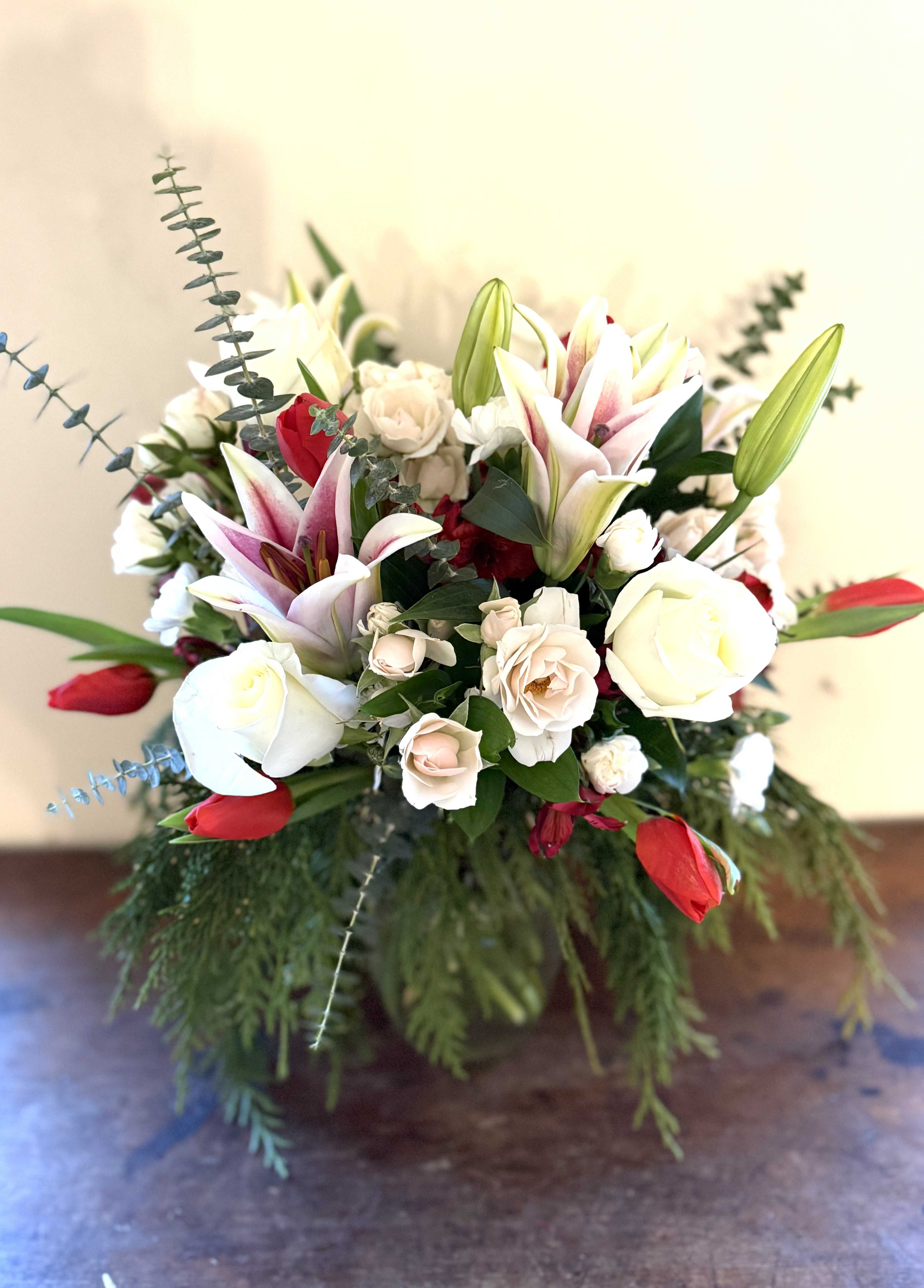 Arrangement of white roses, blush lilies, and red tulips in a clear vase with cascading greenery.