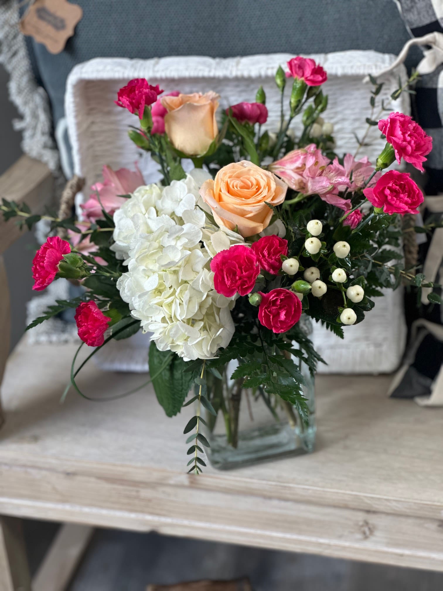 Mixed bouquet of peach roses, white hydrangea, and pink carnations in a glass vase