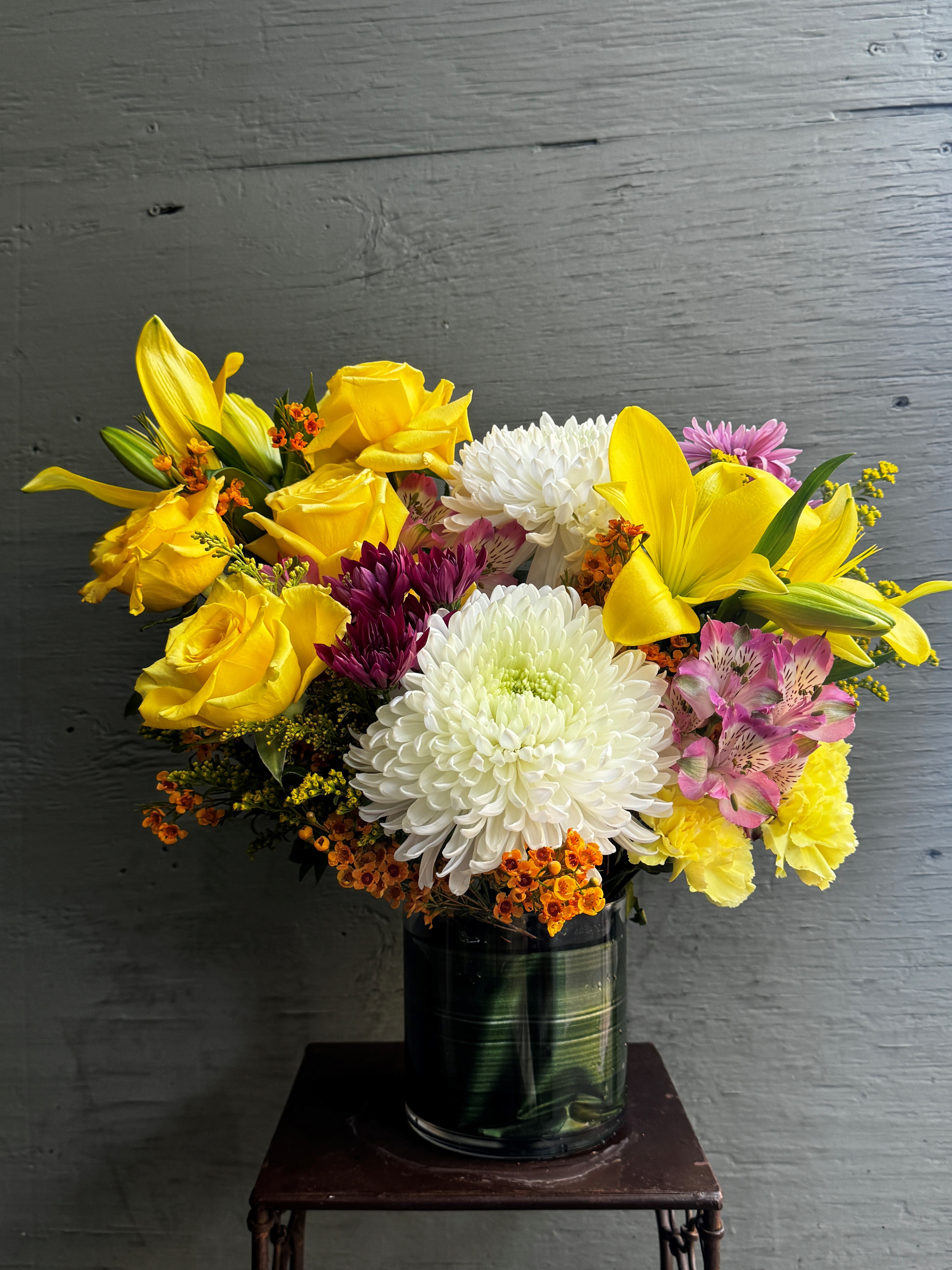 Bouquet of yellow roses, white chrysanthemums, and lilies in a glass vase