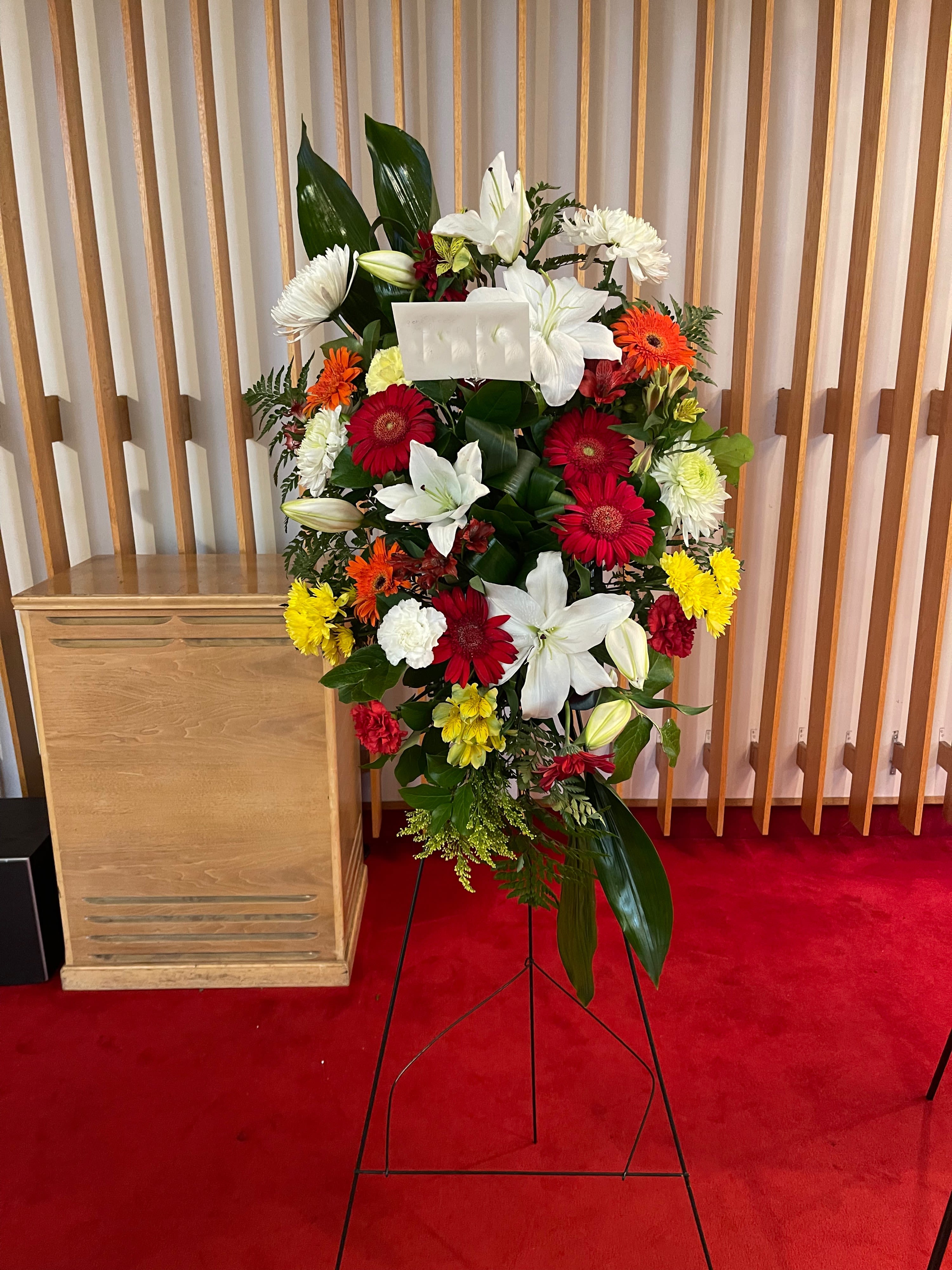 Standing floral spray with white lilies, red gerberas, and yellow blooms