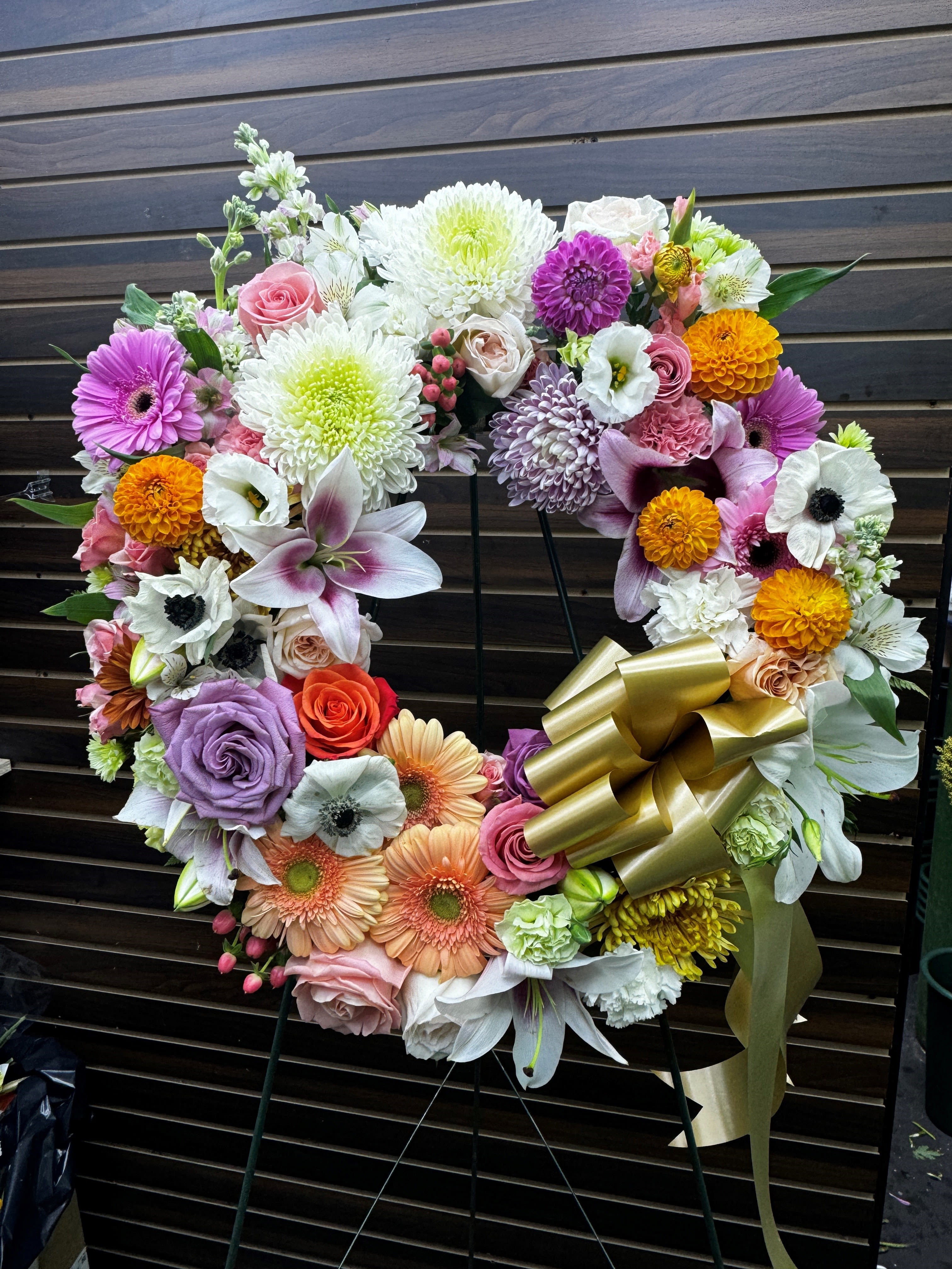 Heart-shaped floral wreath with mixed blooms and a gold ribbon bow