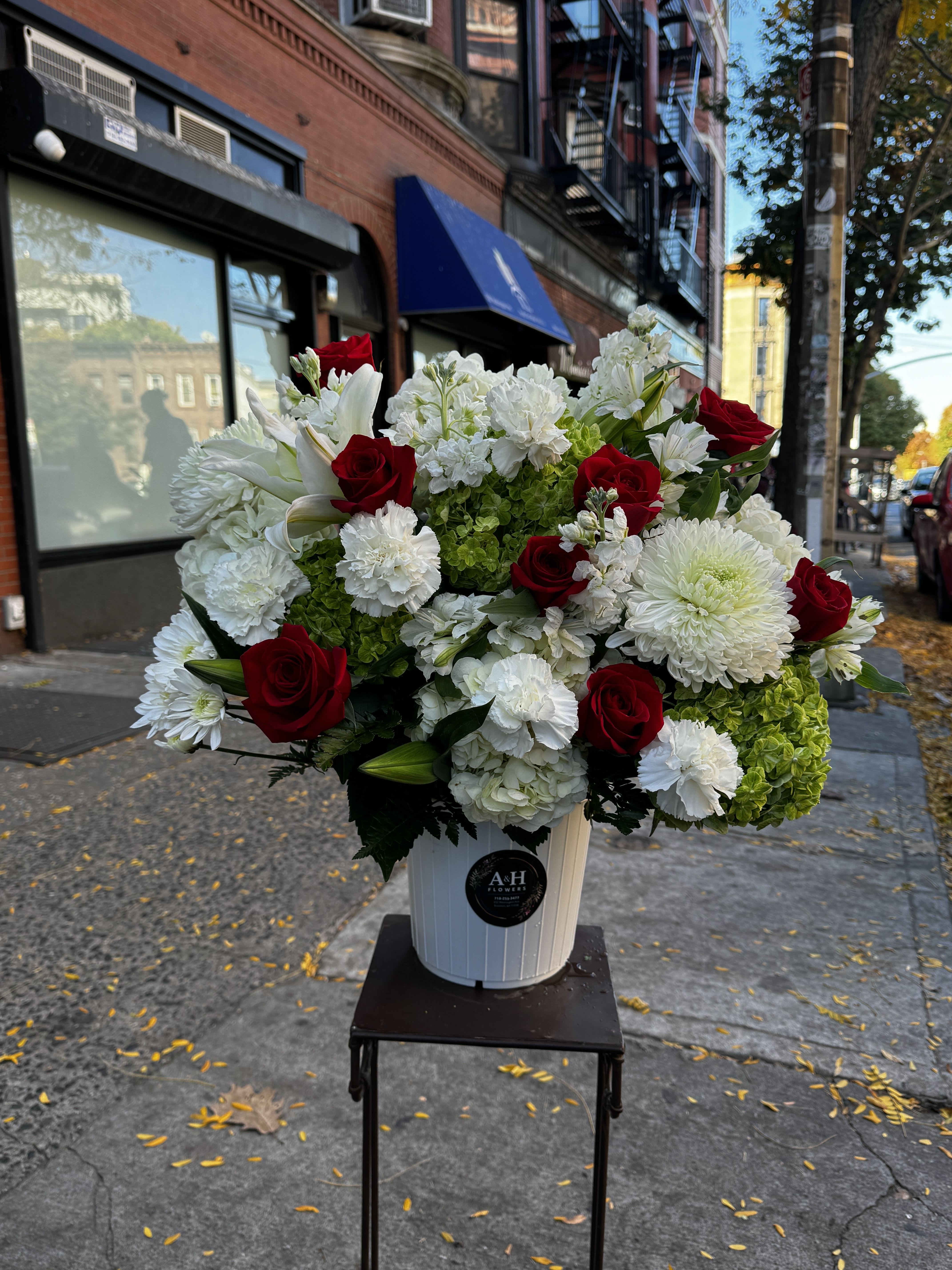 Red roses and white flowers arranged in a white bucket on a stand
