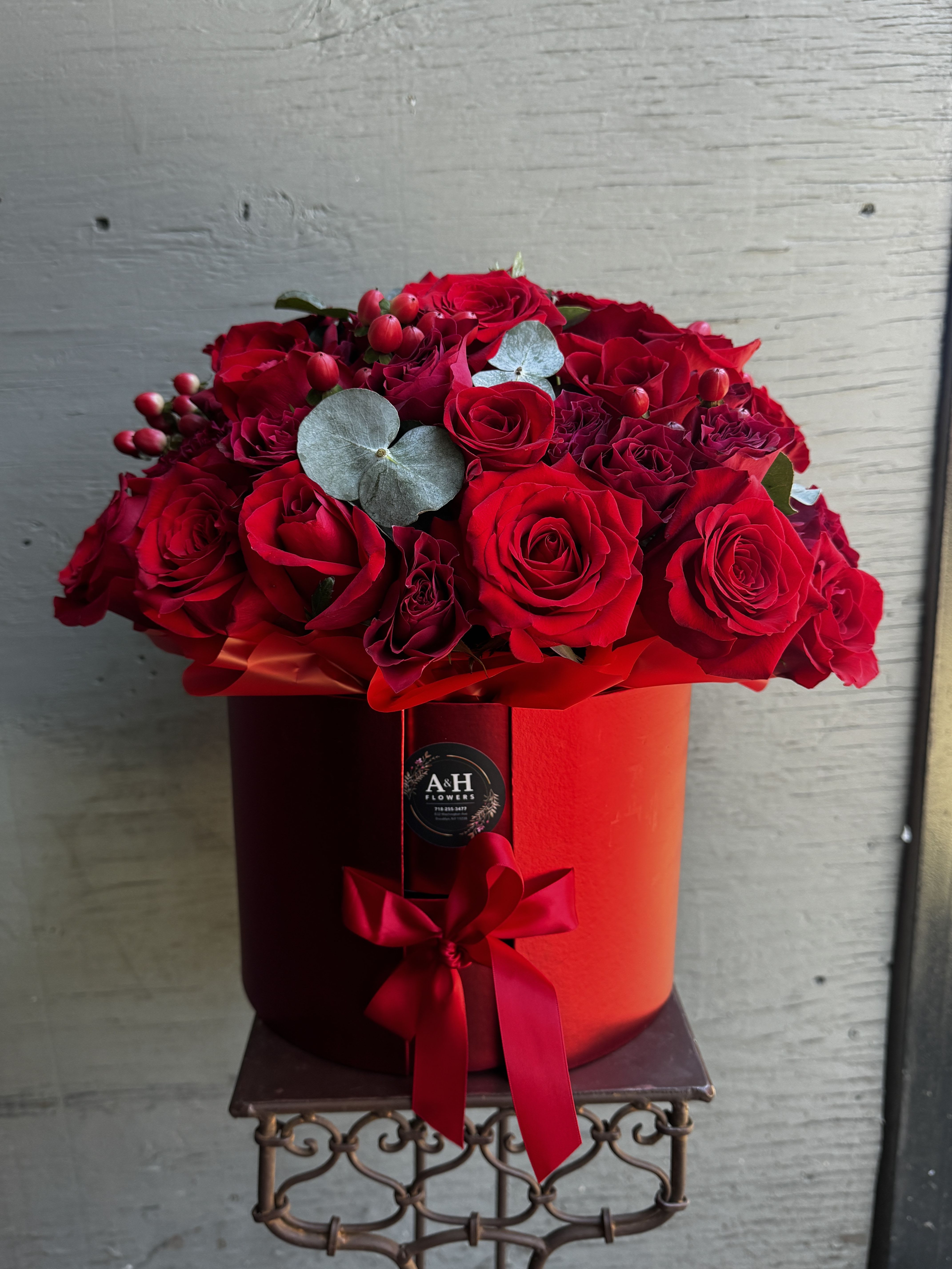 Red roses arranged in a round red hat box with a ribbon