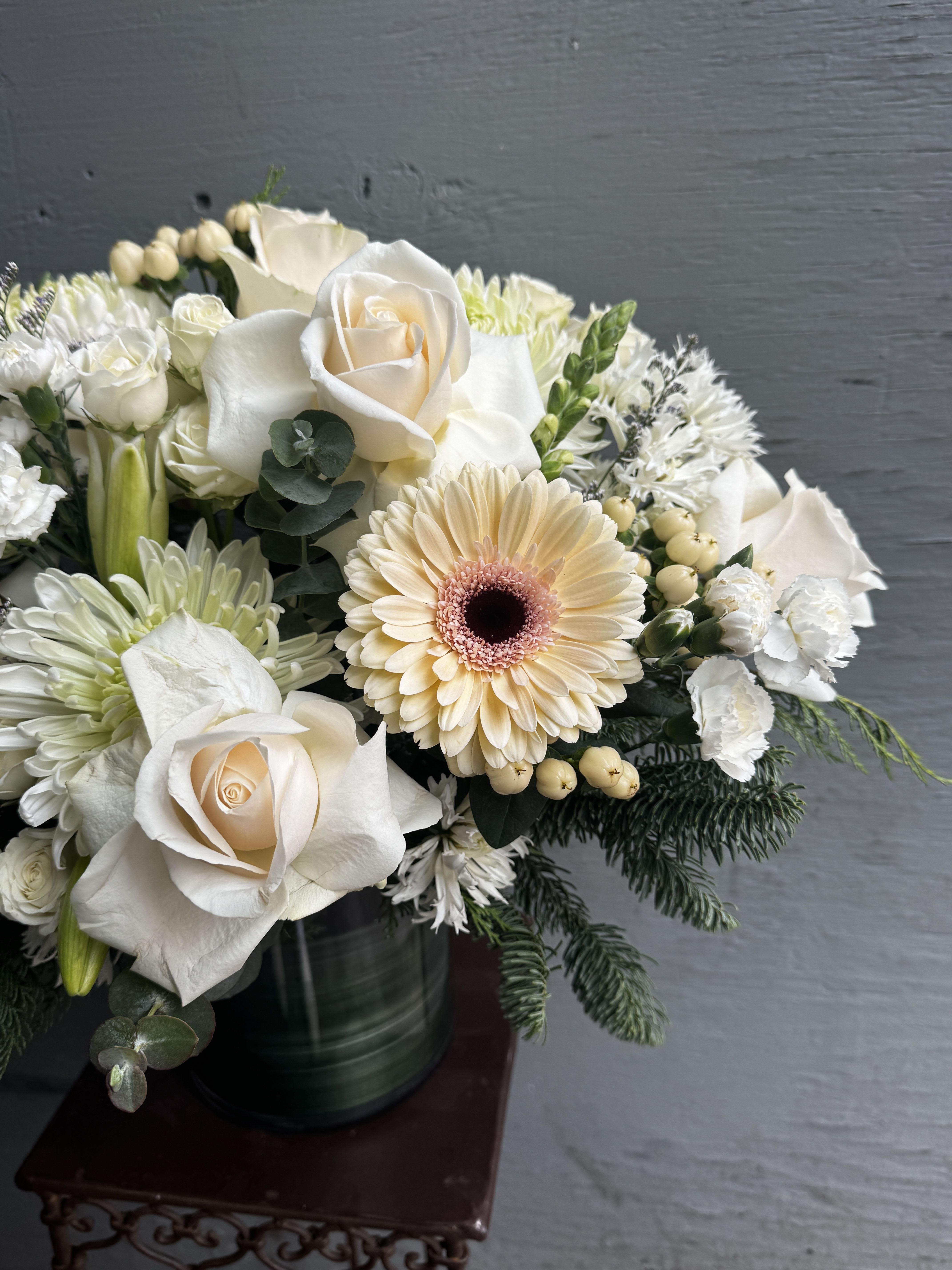 White roses and a pale peach gerbera daisy in a dark vase