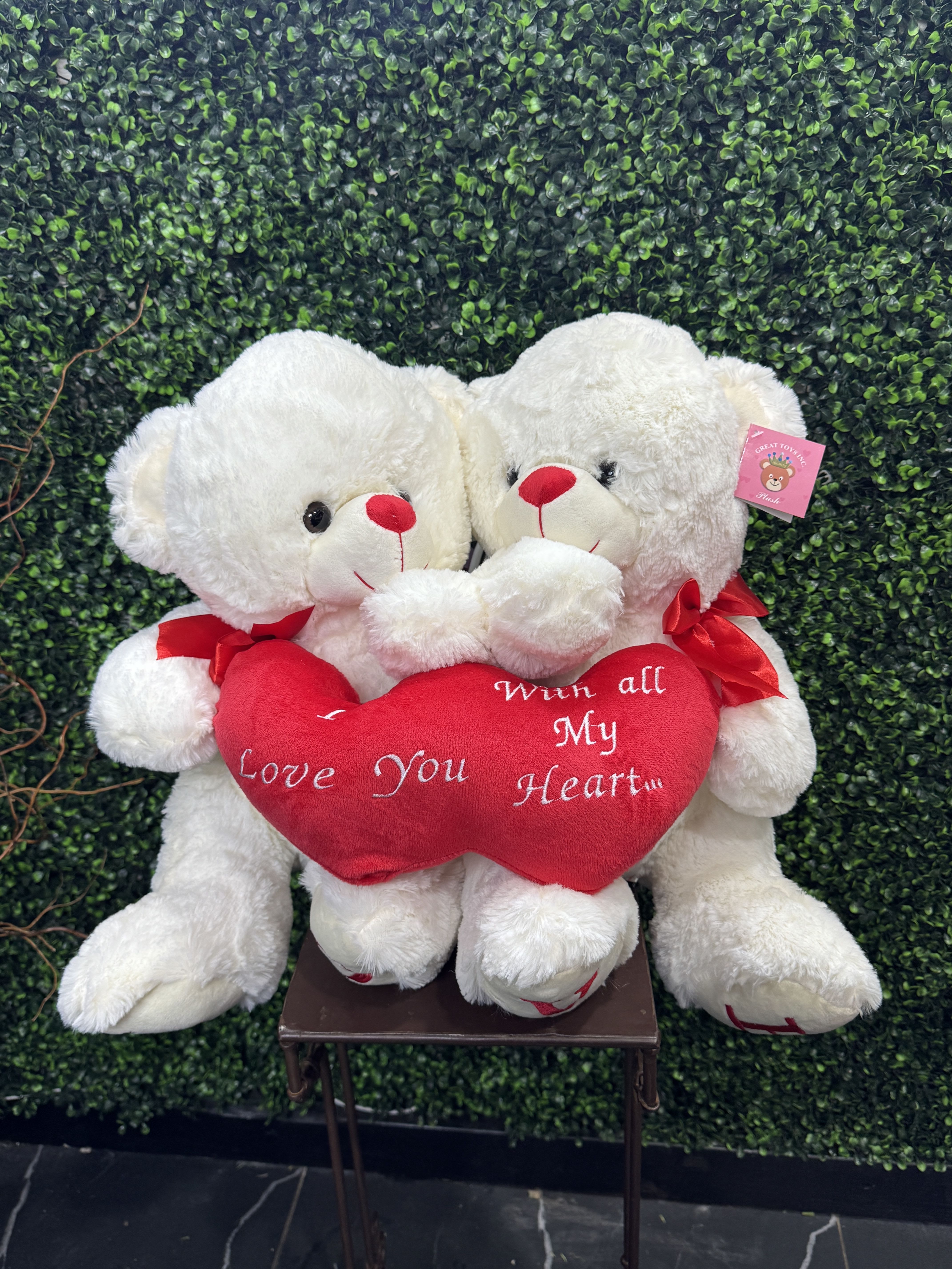 Two white teddy bears holding a red heart pillow