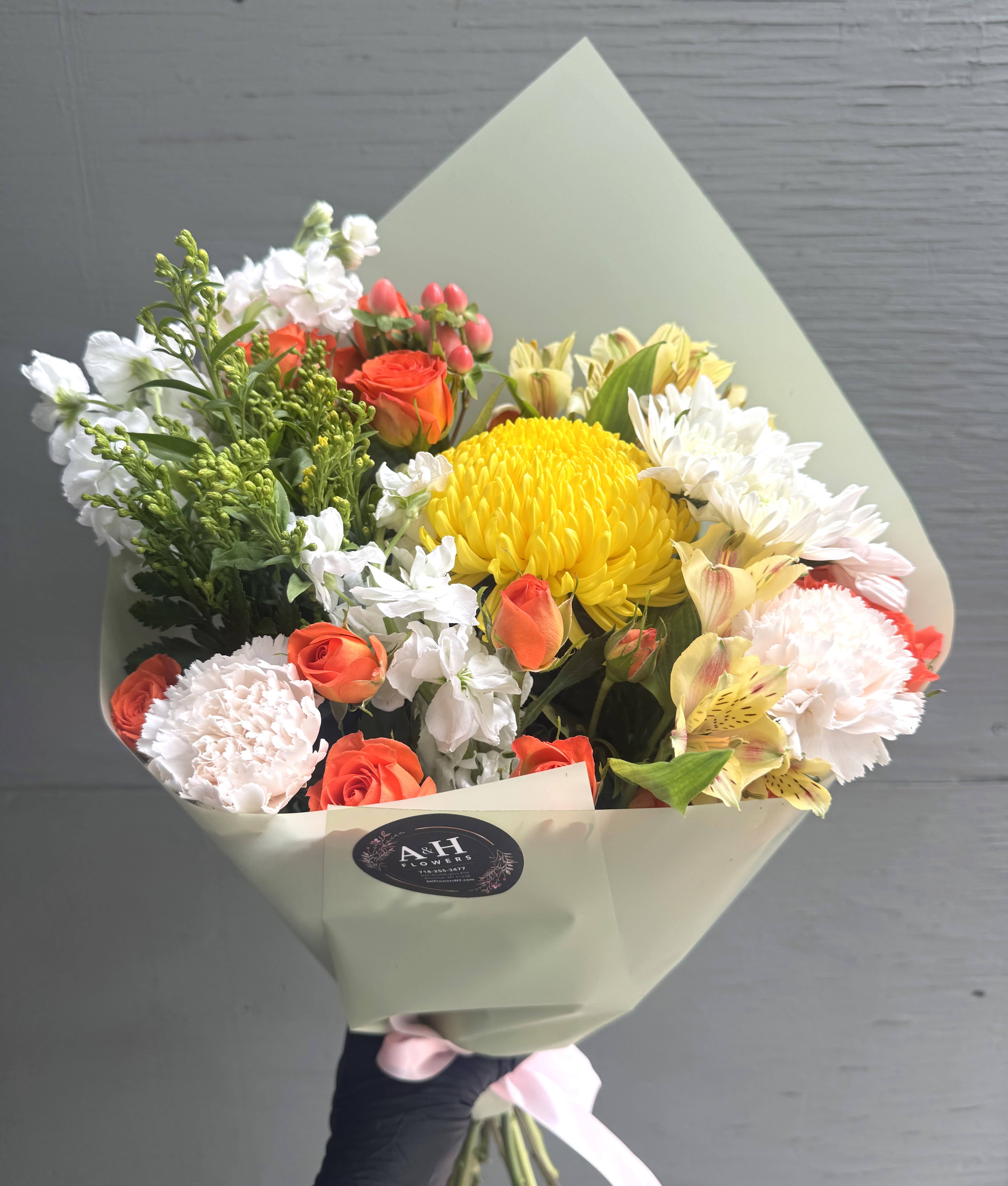 Bouquet of yellow, orange, and white flowers wrapped in pale paper