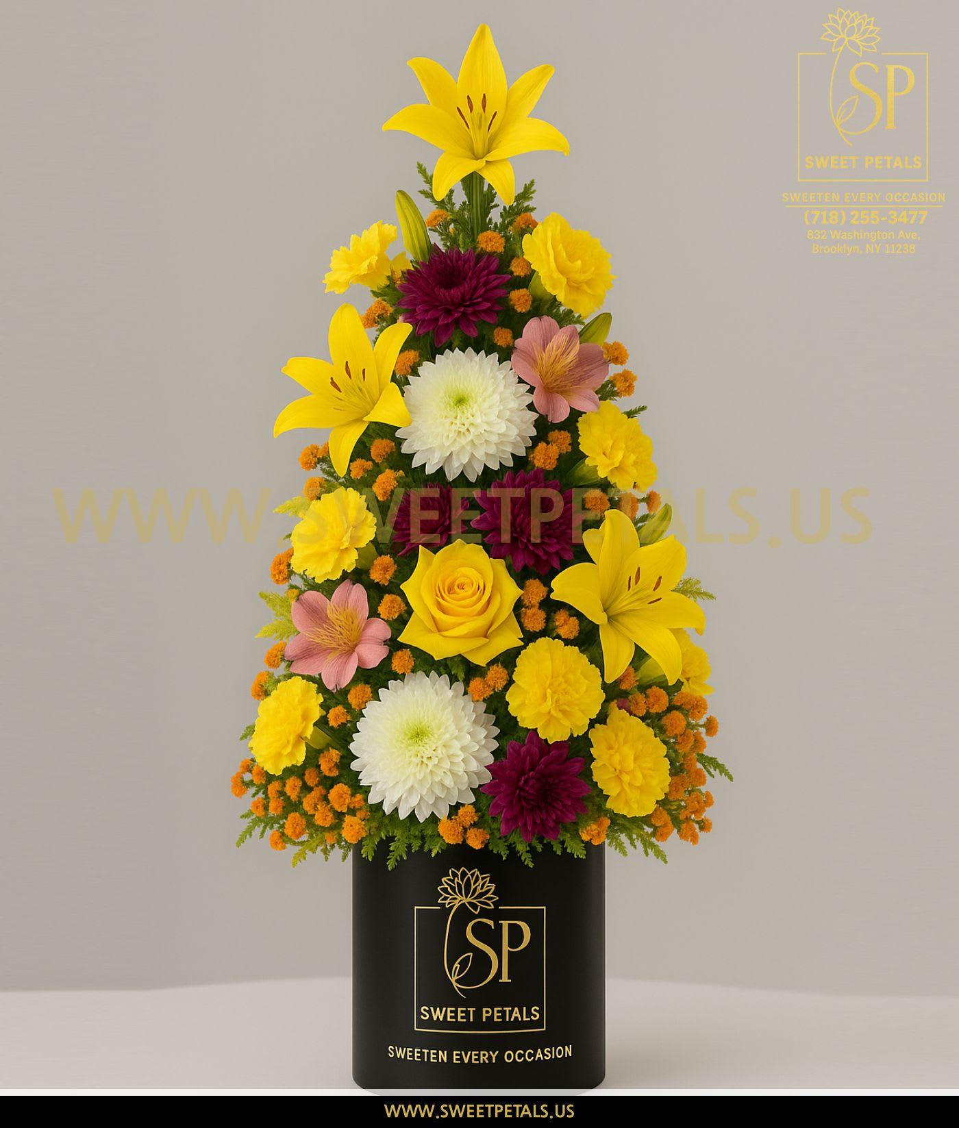 Triangular floral arrangement in a black vase with yellow lilies and mixed blooms