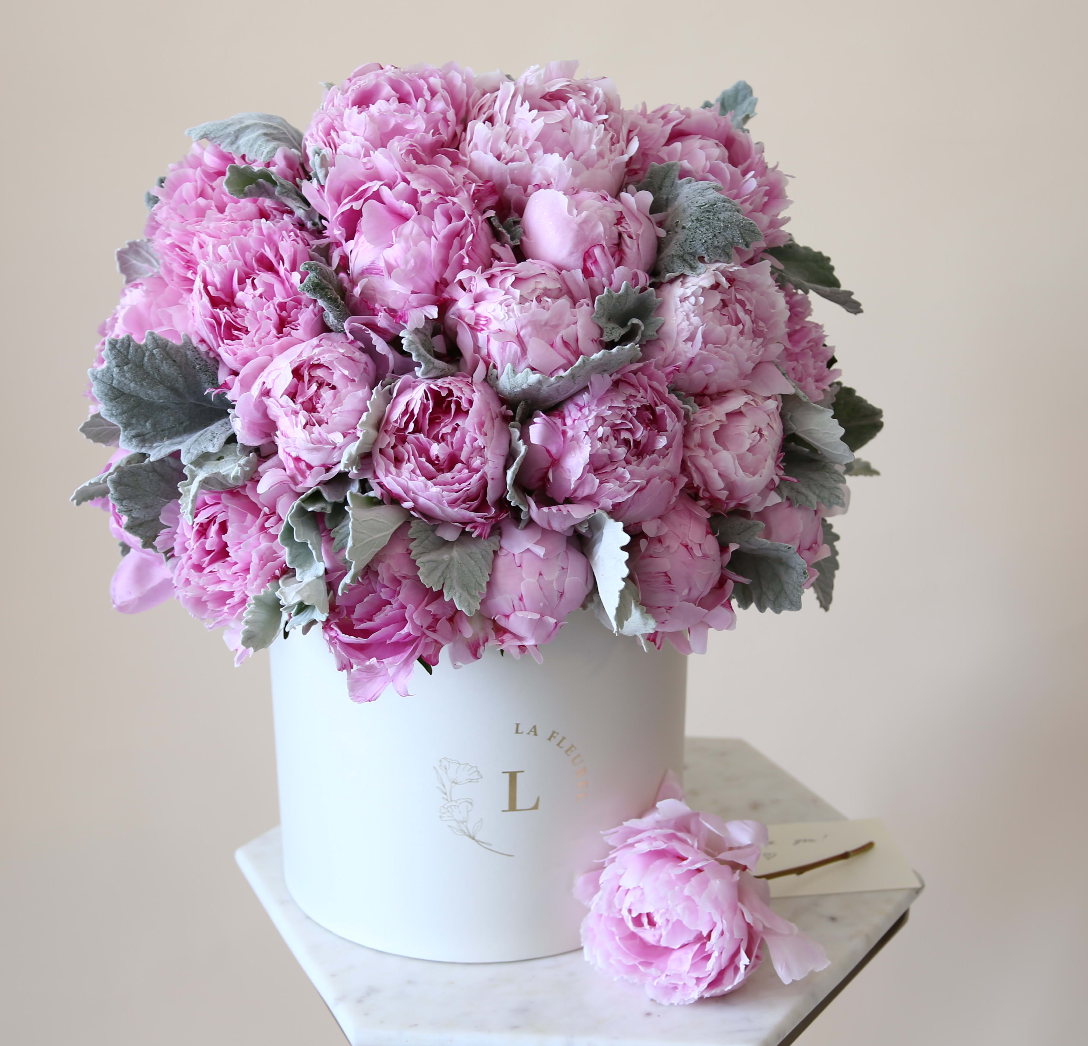 Pink peony bouquet in a white hatbox with a single bloom beside it