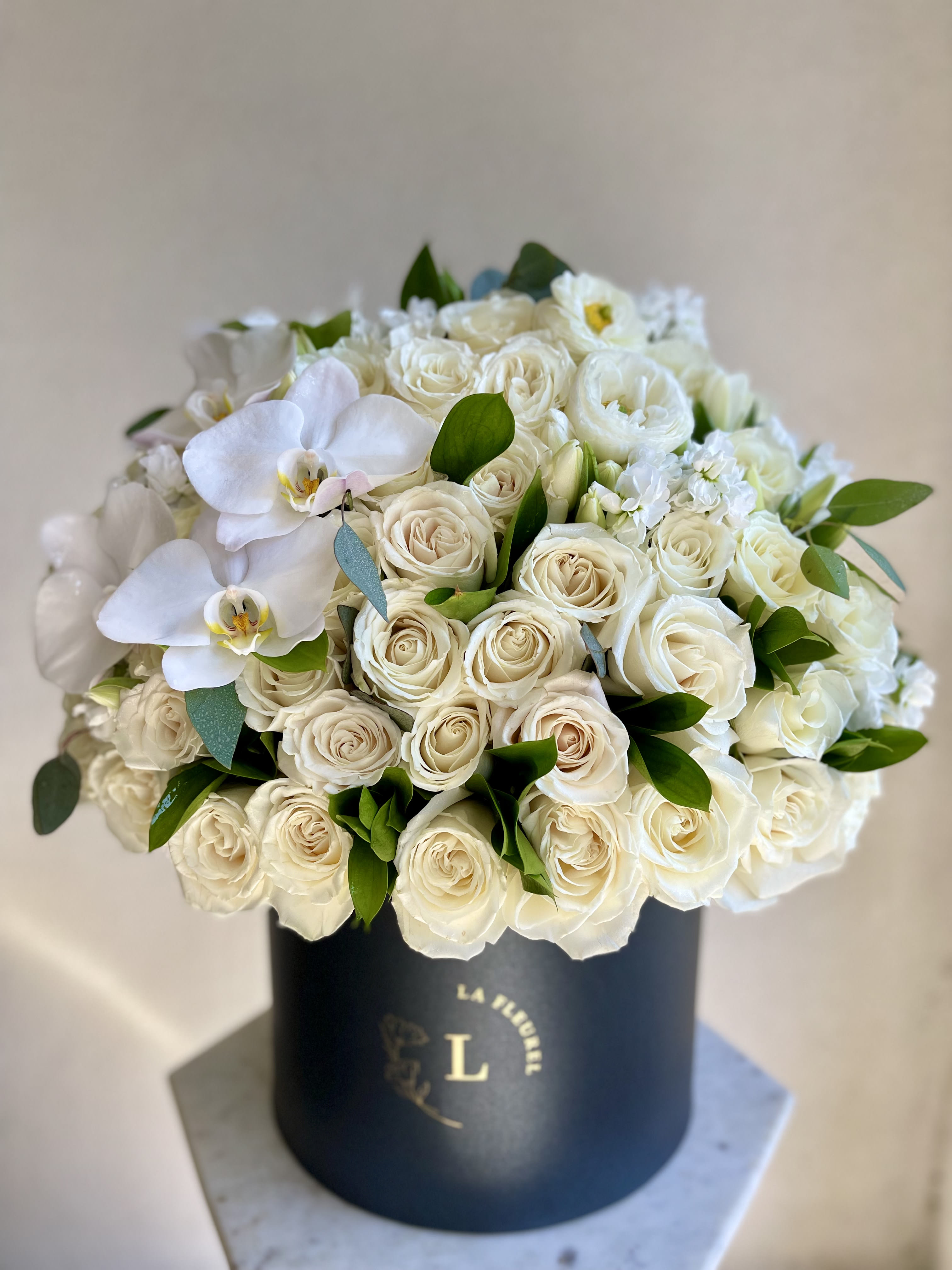White Elegance  - This beautiful arrangement is filled with white roses, tulips and orchids to deliver your special message to your special someone.  Perfect for any occasion. You can choose any color of the box.  Arrangement includes: white roses, tulips and greens Medium box measured at 9.75" Dia. x 9.25" H Custom greeting card   Arrangement includes:  MEDIUM BOX Custom greeting card