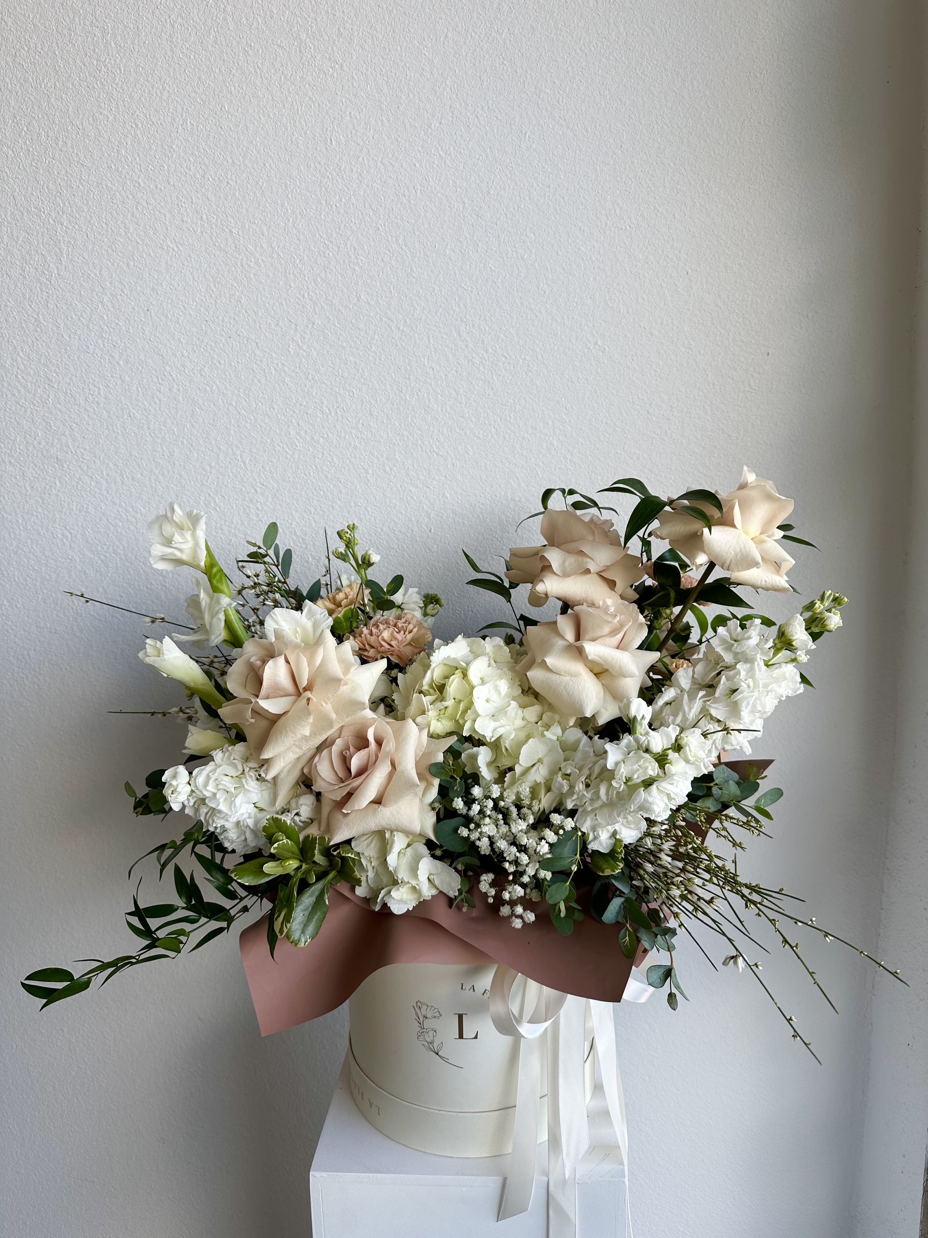 Creme Brûlée - This beautiful arrangement is filled with beige roses, hydrangeas, carnations and greens to deliver your special message to your special someone.  Perfect for any occasion. You can choose any color of the box.  Arrangement includes: white roses, hydrangea, carnations and dusty miller Medium box measured at 9.75" Dia. x 9.25" H Custom greeting card