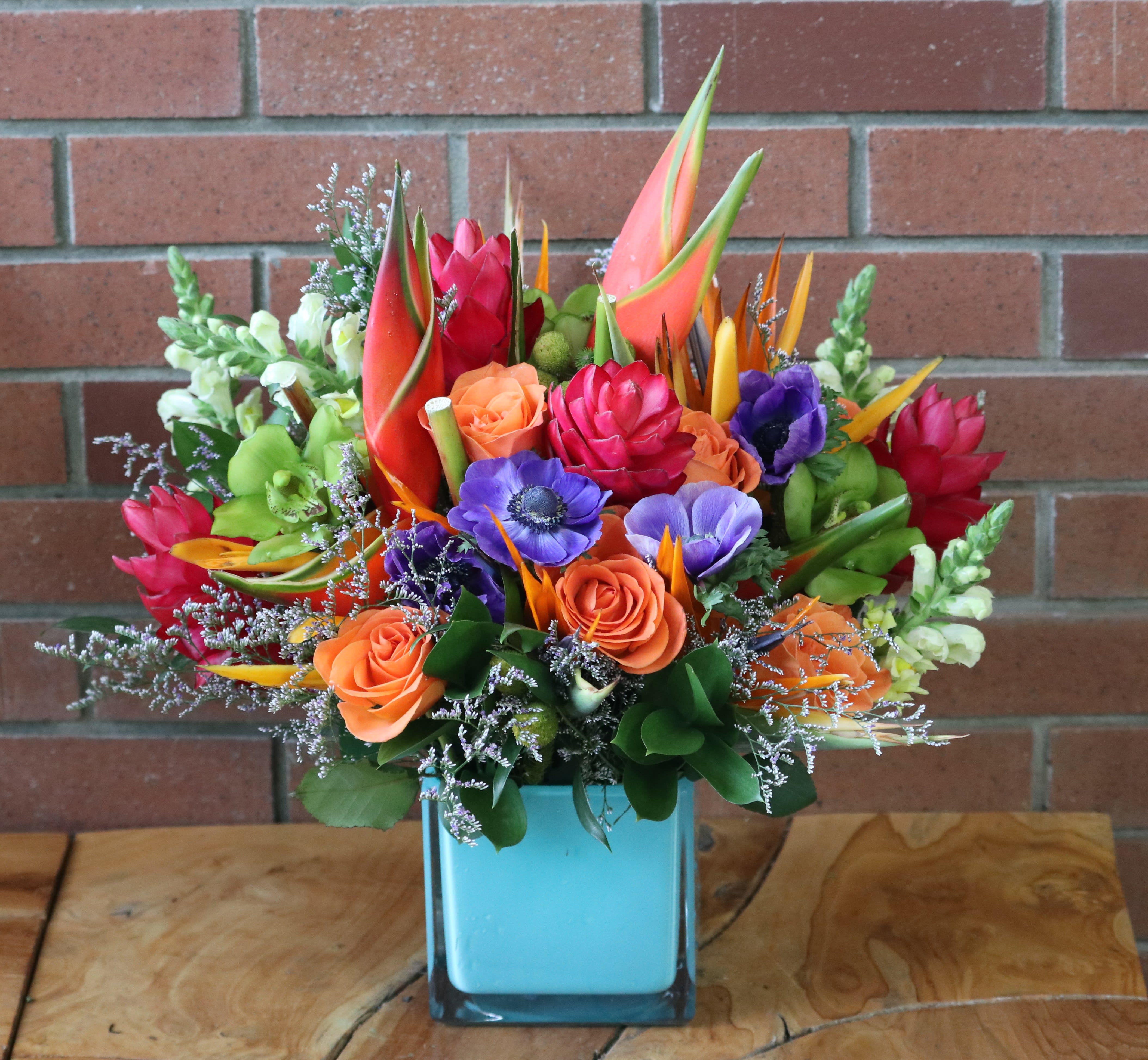 Have A Tropical Day Bouquet Have A Tropical Day Bouquet - Gorgeous tropical assortment of flowers - premium heliconia, birds of paradise, orchids, anemones, orange roses, snaps, ginger greens and filler in a modern cube vase