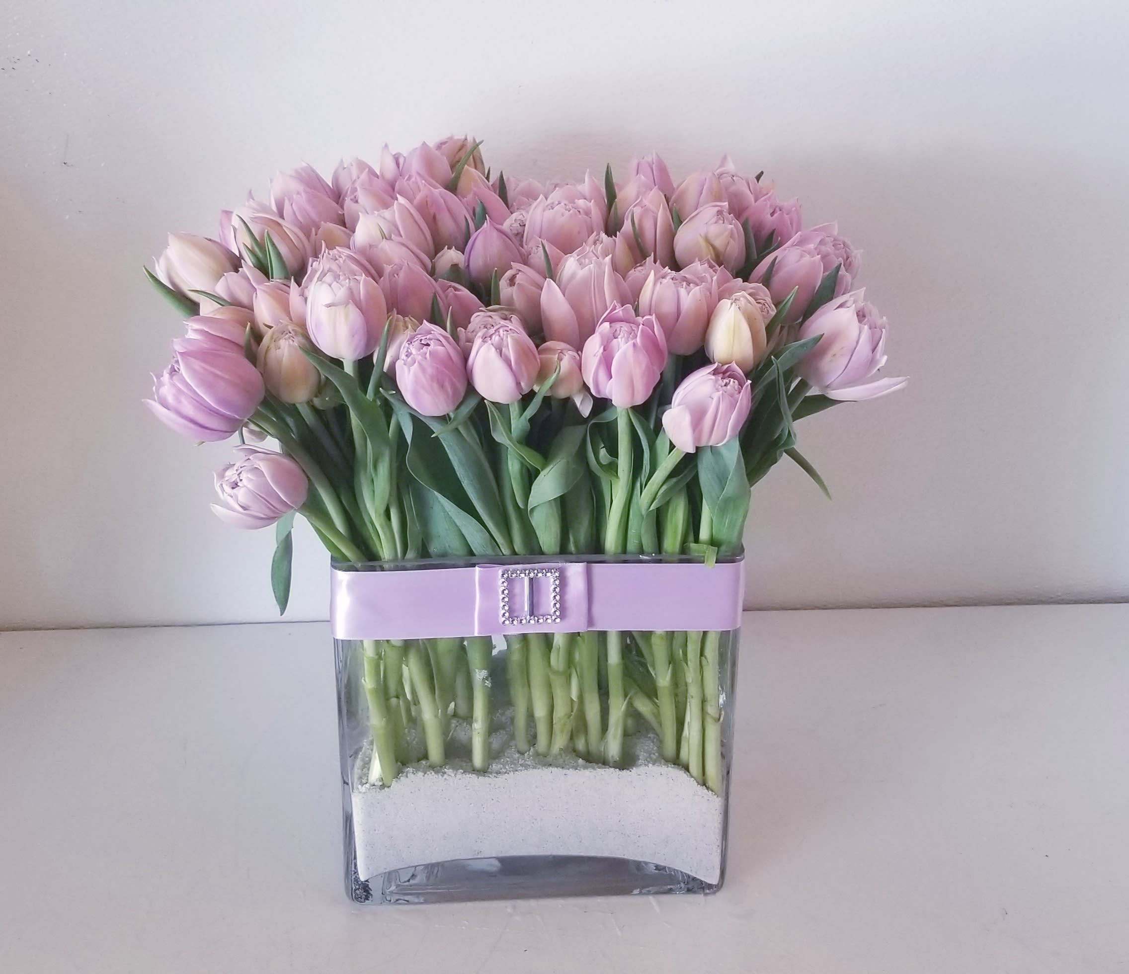 Mademoiselle Mademoiselle - Lavish pinkish lavender parrot tulips designed in a flat square vase with sand at the bottom.