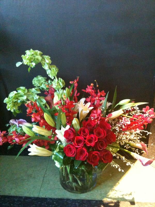 Love swept - Lovely array of roses, lilies, belles of ireland, orchids and other season flowers. Done in gorgeous red, green, and white tones.  Designed in a clear glass vase.
