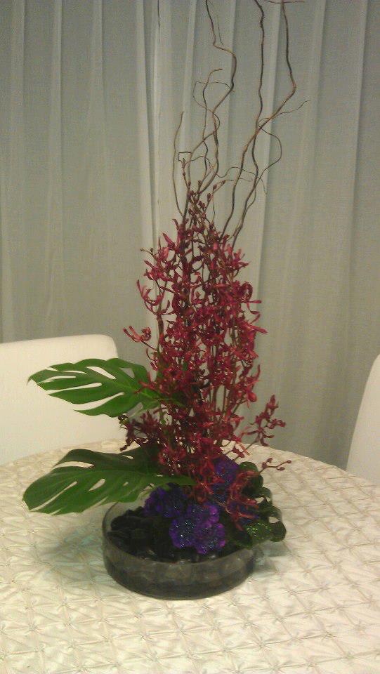 Orchids of Plenty Orchids of Plenty - Mono-Floral design style a grouping of orchids, with paved floral product in base, accented with rocks, curly willow, & tropical foliage.