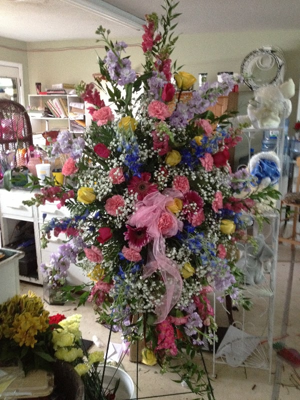 Vibrant Standing Spray Vibrant Standing Spray - * Pink Snaps * Lavender Stock * Pink Roses * Yellow Roses * Pink Carnations * Blue Delphinium * Assorted Pink Gerber Daisies * Baby's Breath * Assorted Greenery such as Ruskus, Myrtle and others * Pink bow * 54"- 60" green metal easel This colorful standing spray is the perfect way to show sympathy. We offer alternate color schemes.