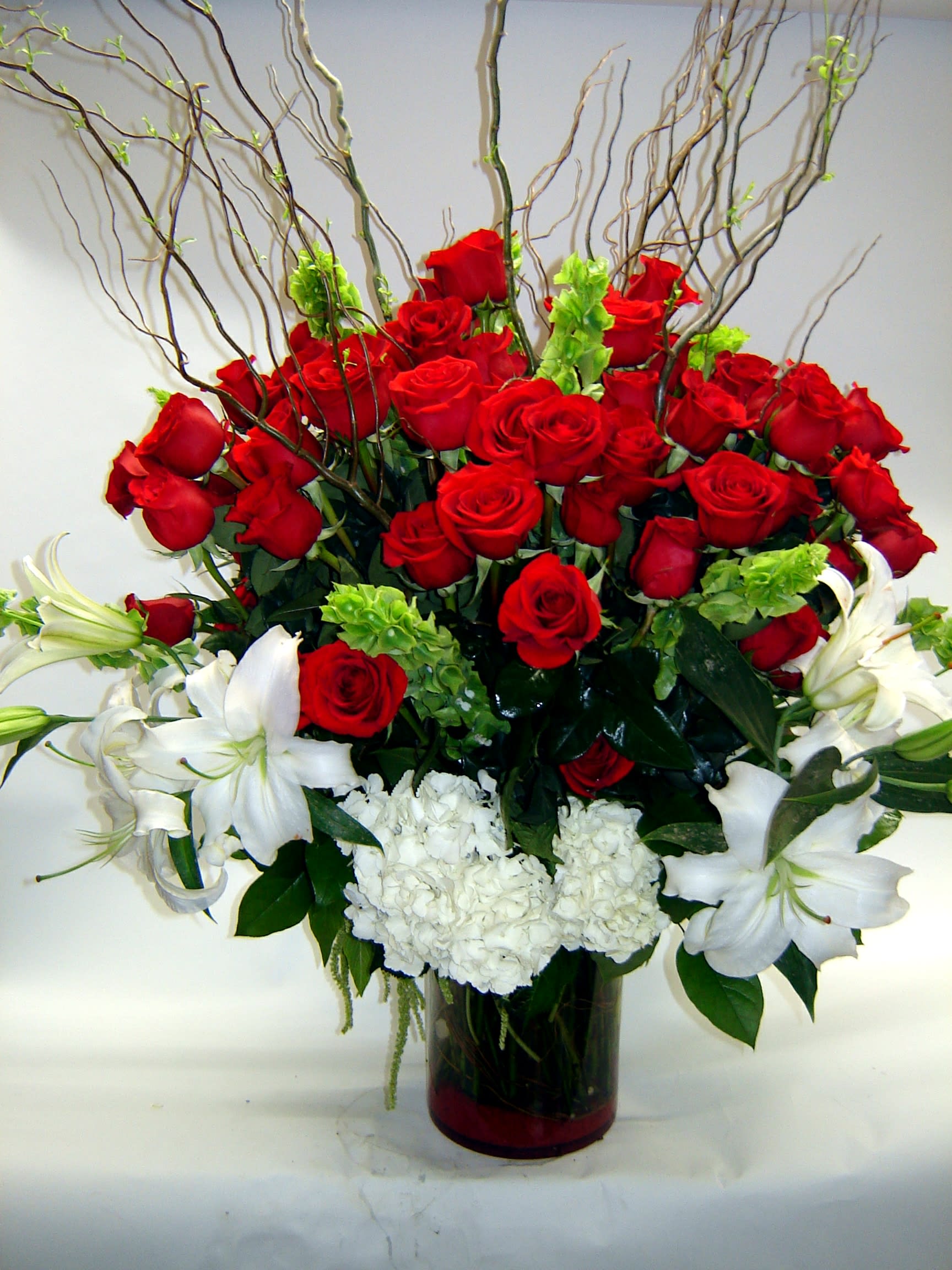 Red Rose Bliss Red Rose Bliss - Four dozen red roses elegantly arranged in a large clear cylinder vase with hydrangea, Casablanca lilies, bells of Ireland and curly willow. Color Rose substitutions are available for this arrangement