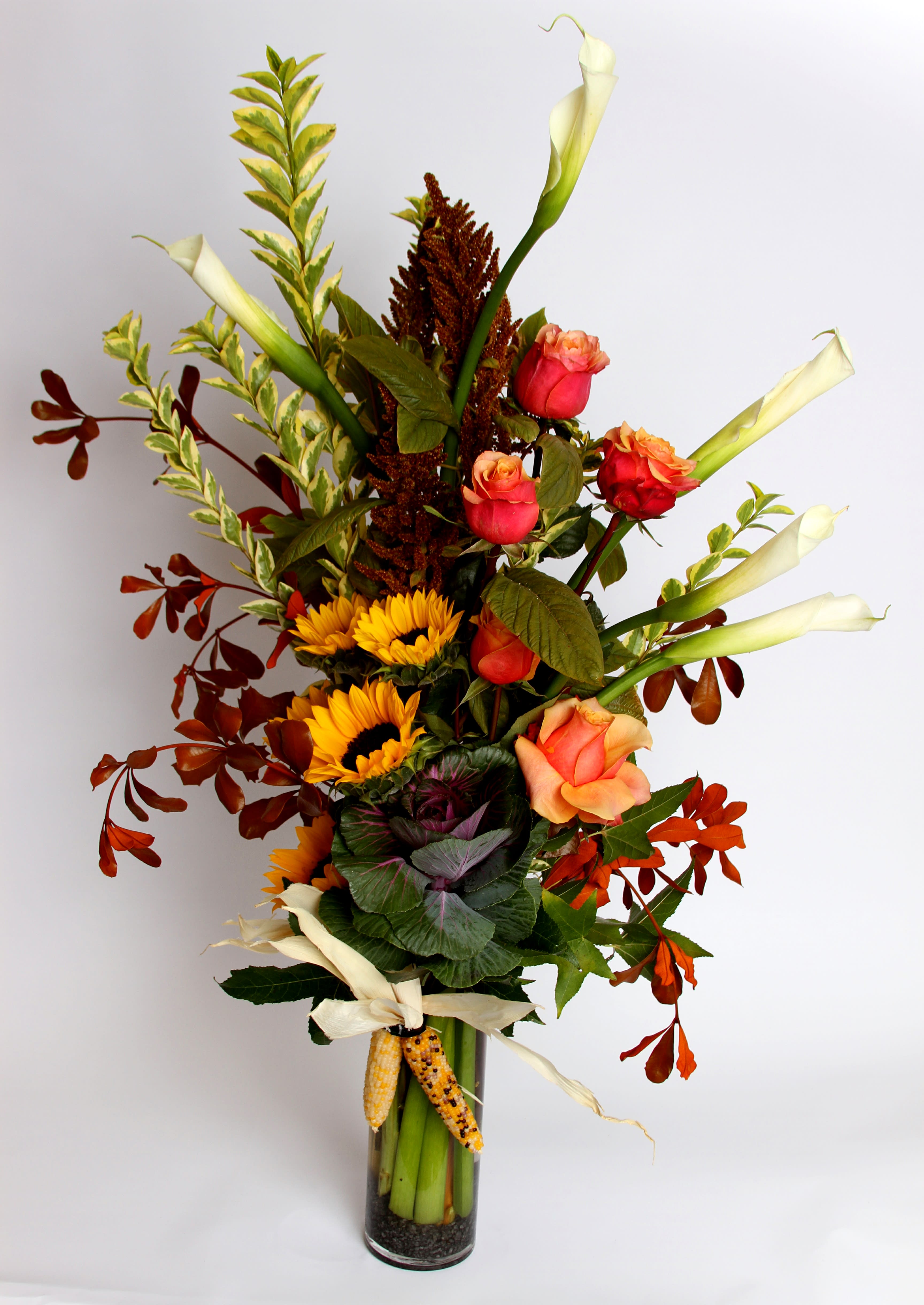 Reaching Lilies Reaching Lilies - An elegant, yet festive vase arrangement from our Fall Collection with Calla Lilies, sunflowers, roses, kale and harvest corn