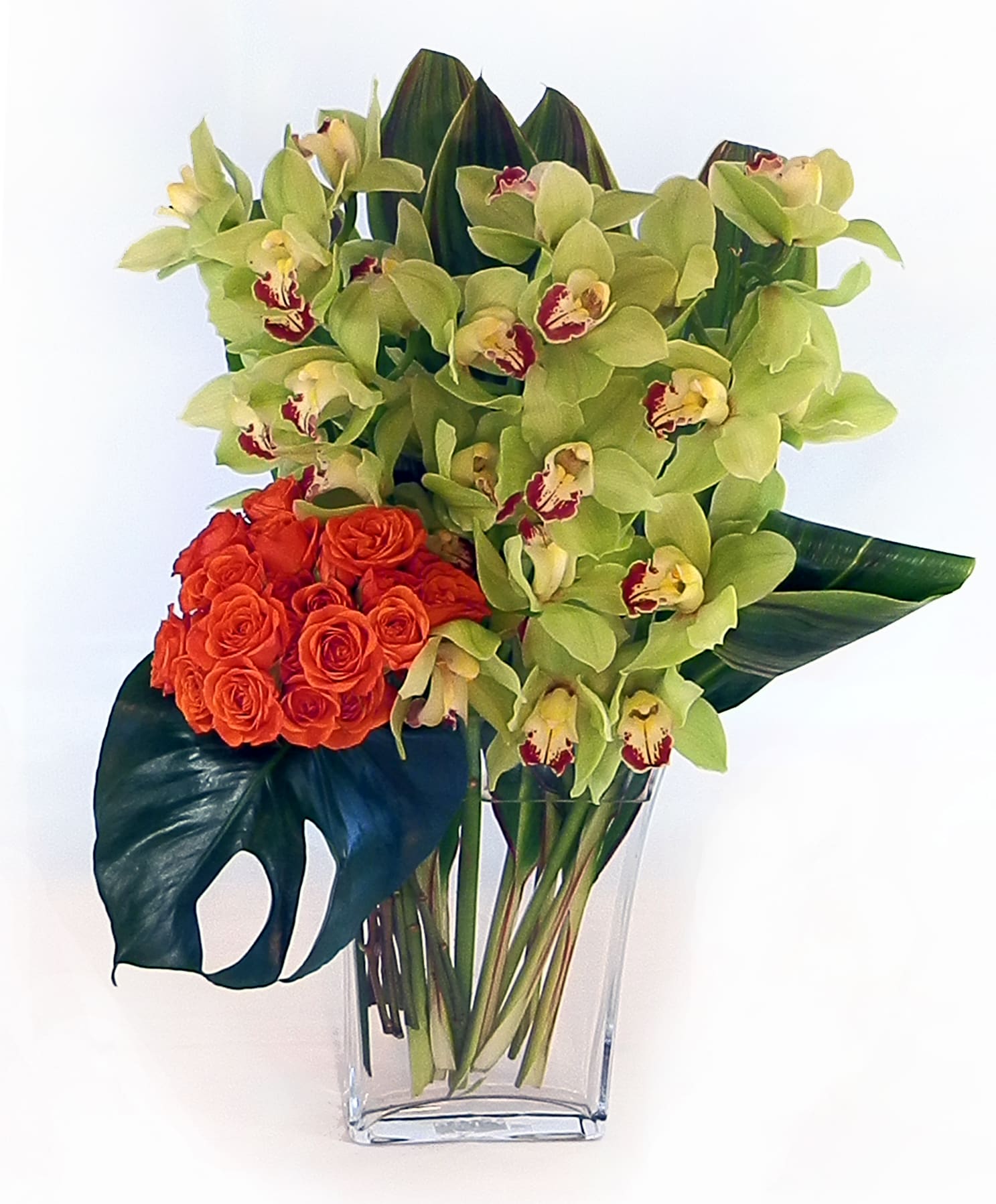 Distinction Distinction - Luxurious combination of orchids and roses with tropical foliage in a heavy glass rectangular vase.