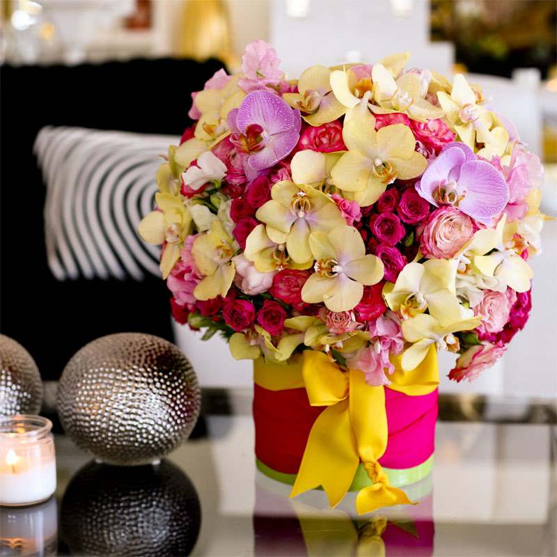 Sugar and Spice - Colorful display of pale yellow Phaelonopsis orchids, fuschia mini roses, and soft pink roses in a bright fabric-wrapped glass vase.  