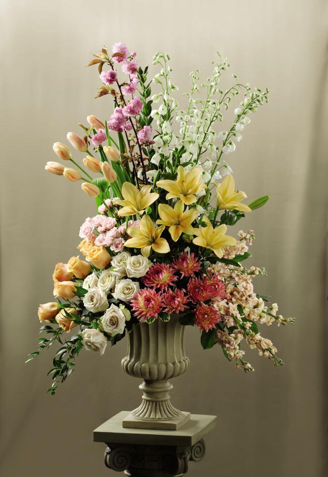Colorful  Altar Arrangmeent - This  Altar Arrangement blooms with the colors of  happiness and grace to celebrate your wedding day. Peach tulips, peach roses, white roses, peach stock, dark pink dahlias, white delphiniums, pink spray roses, peach Asiatic Lilies, pink flowering branches and an  assortment of fresh, lush greens are beautifully arranged in a resin urn and displayed on a 3-inch pedestal to brighten the alter during your  ceremony. Approx. 48âH x 30âW.