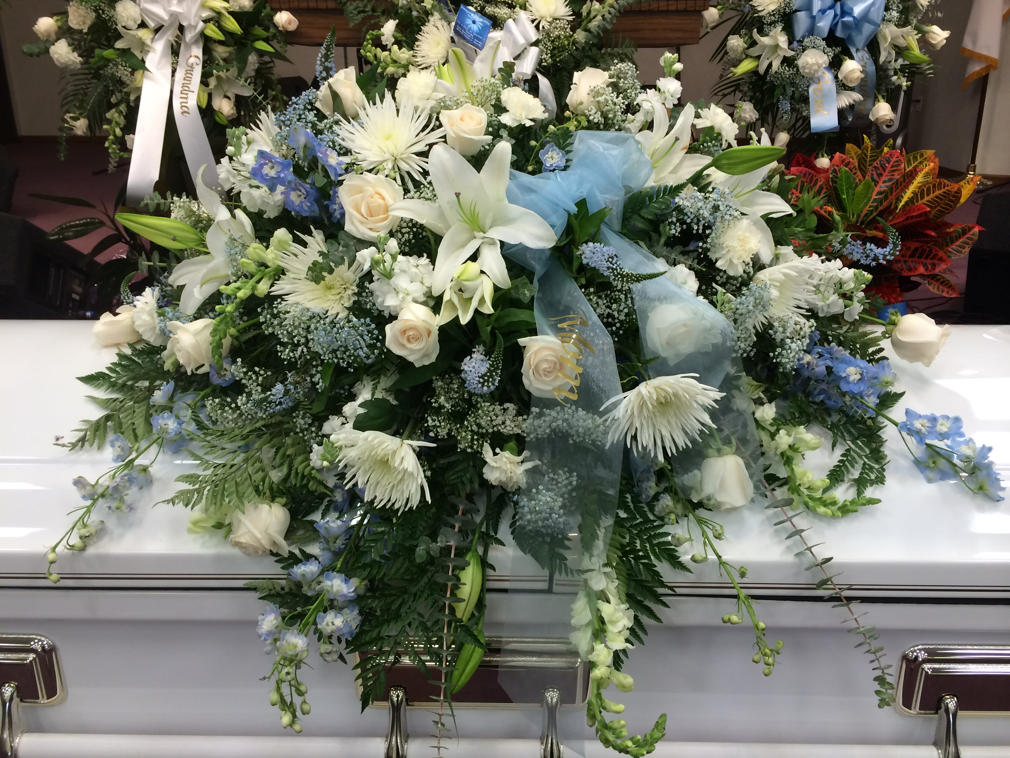 Pale Blue & White Casket Spray Pale Blue & White Casket Spray - Mixed varieties of white flowers, some sprayed pale blue with wispy pale blue ribbon