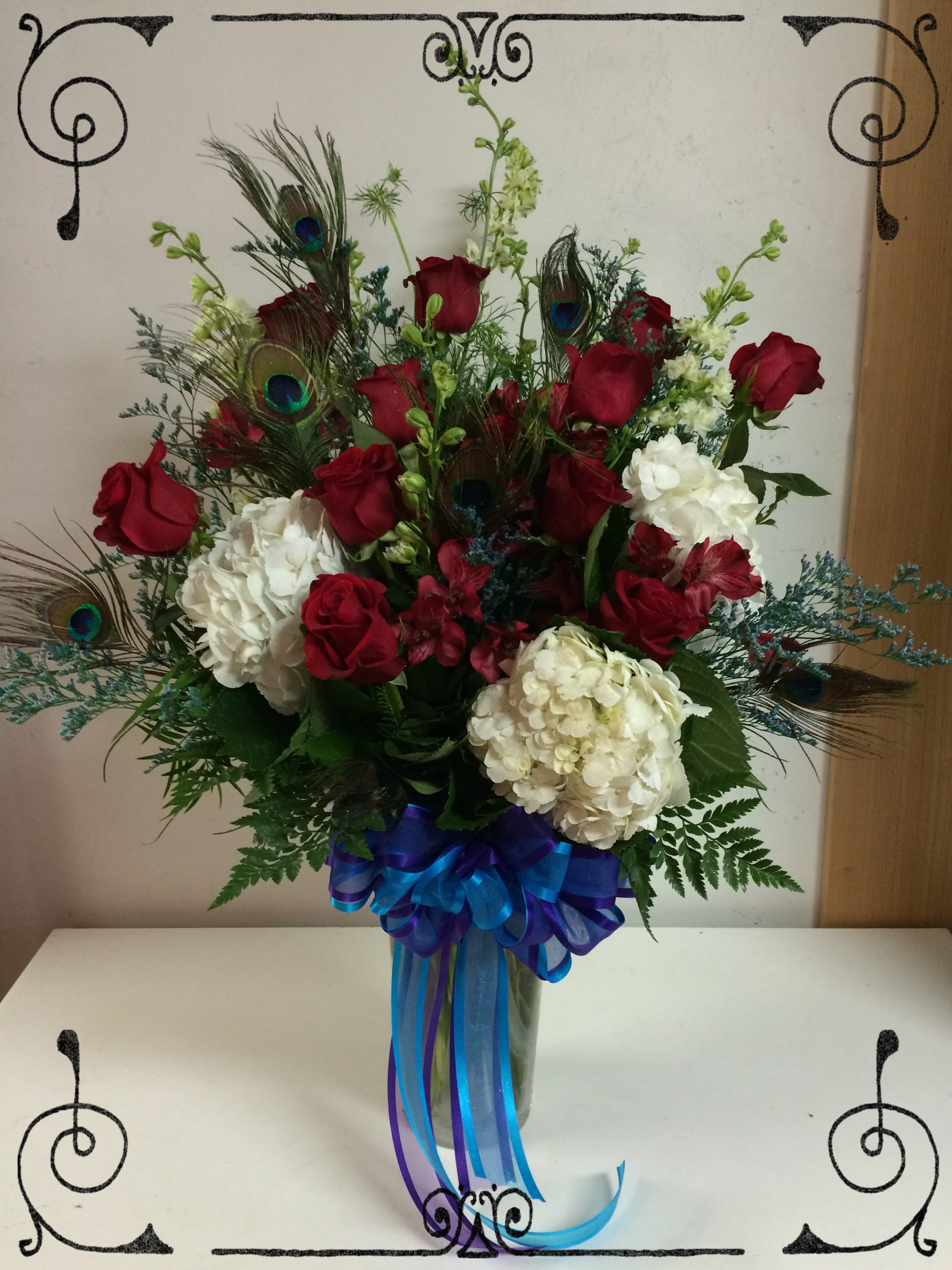 Peacock Roses &amp; Hydrangeas - A dozen red roses and 3 white hydrangeas in a tall clear glass vase with peacock feather accents