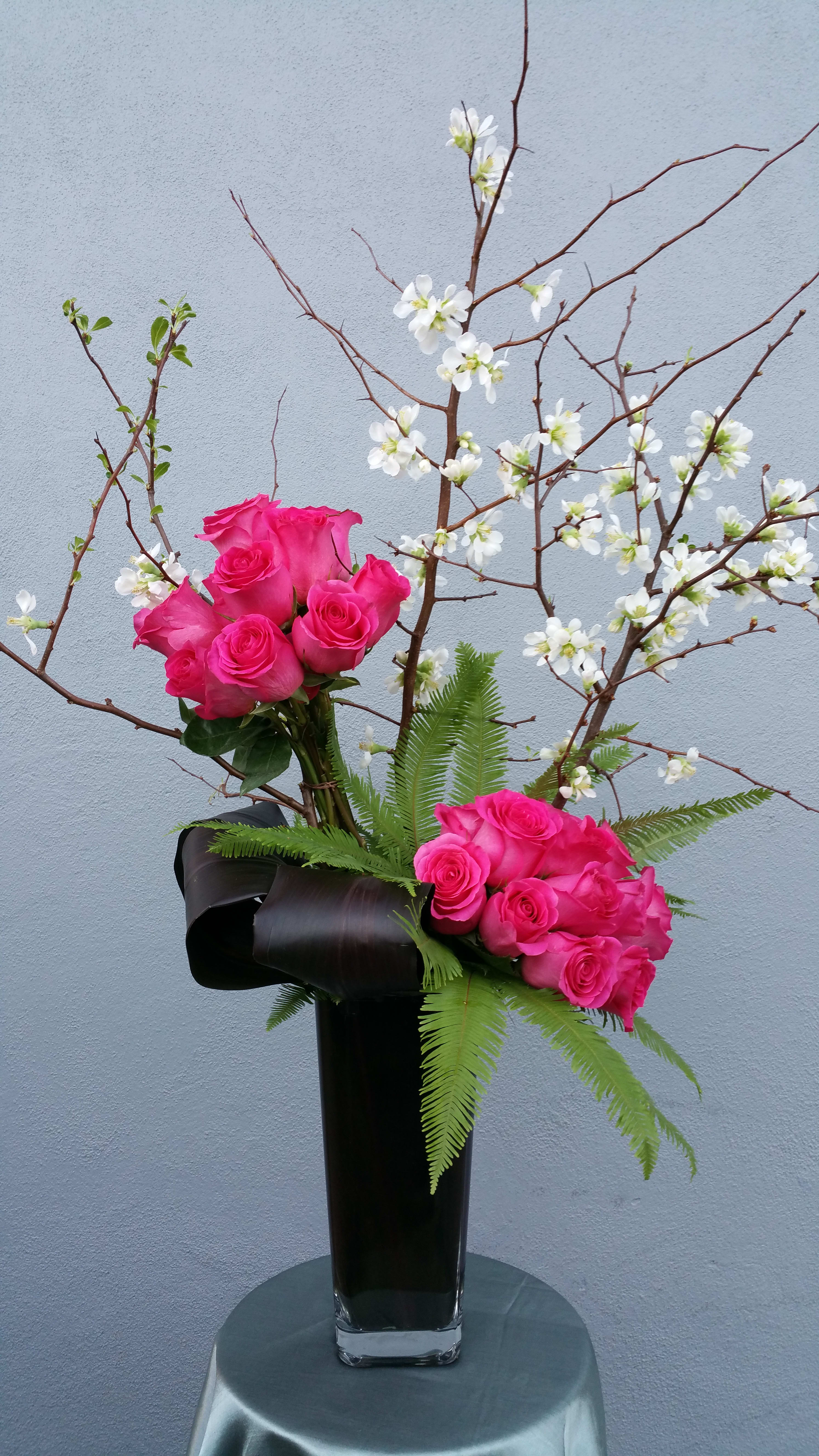 Pink roses in a tall black vase with white blossoms on branches