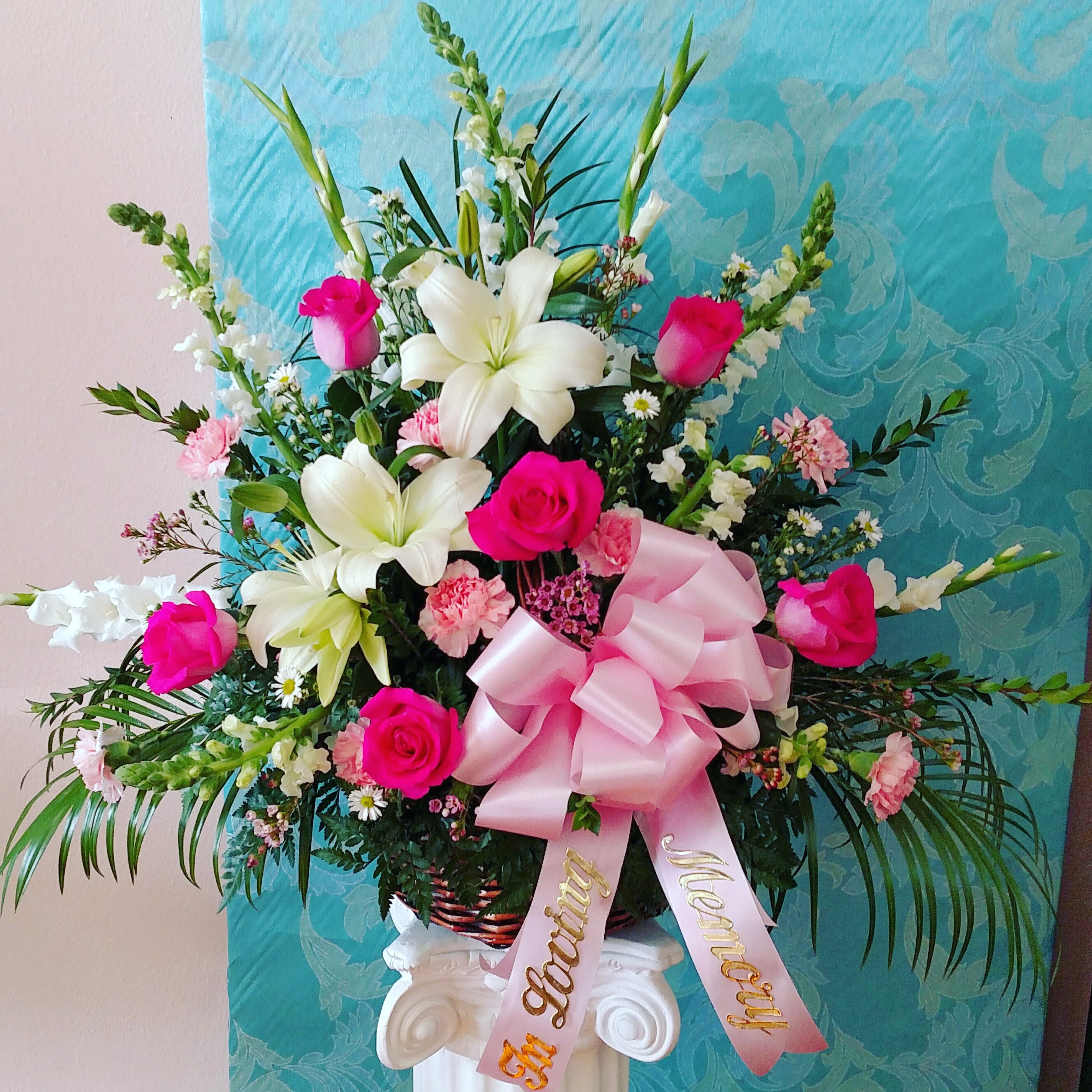 In Loving Memory Pink Basket - This whicker basket has large hot pink roses, white gladiola, lilies and snap dragon as well as light pink carnations and other fuller flowers. Banner Bow is included.