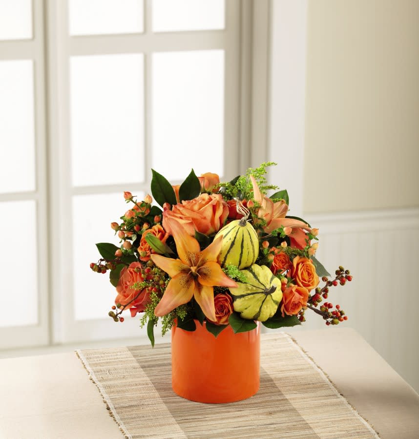 The FTD Vibrant Views Bouquet - Blooming with a vibrant light that can't be denied, this brilliant fall flower bouquet is ready to lift any mood and raise any spirit throughout the autumn months ahead. Swirling orange roses, orange spray roses, and star-shaped peach Asiatic Lilies are surrounded with the eye-catching textures of yellow solidago, bittersweet stems, aralia leaves and lush greens with brilliant yellow gourd accents tucked in a just the right spot, all beautifully arranged in an orange ceramic cylinder vase. A wonderful fall birthday, get well, thank you, or happy harvest gift!