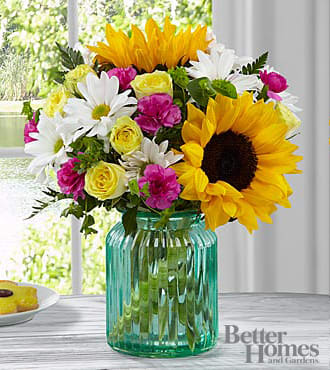 The FTD® Sunlit Meadows™ Bouquet by Better Homes and Gardens® The FTD® Sunlit Meadows™ Bouquet by Better Homes and Gardens® - HG1S FTD® proudly presents the Better Homes and Gardens® Sunlit Meadows™ Bouquet. Blossoming with bright beauty and color palette that exudes charm and cheer at every turn, this bouquet will be that perfect gift for any of life's special moments. Brilliant sunflowers are simply dazzling settled amongst yellow spray roses, magenta mini carnations, white traditional daisies, and lush greens to create a bouquet that has that "fresh from the garden" look. Presented in an aqua blue designer glass vase, this mixed flower bouquet will make an excellent birthday, thank you, or get well gift.
