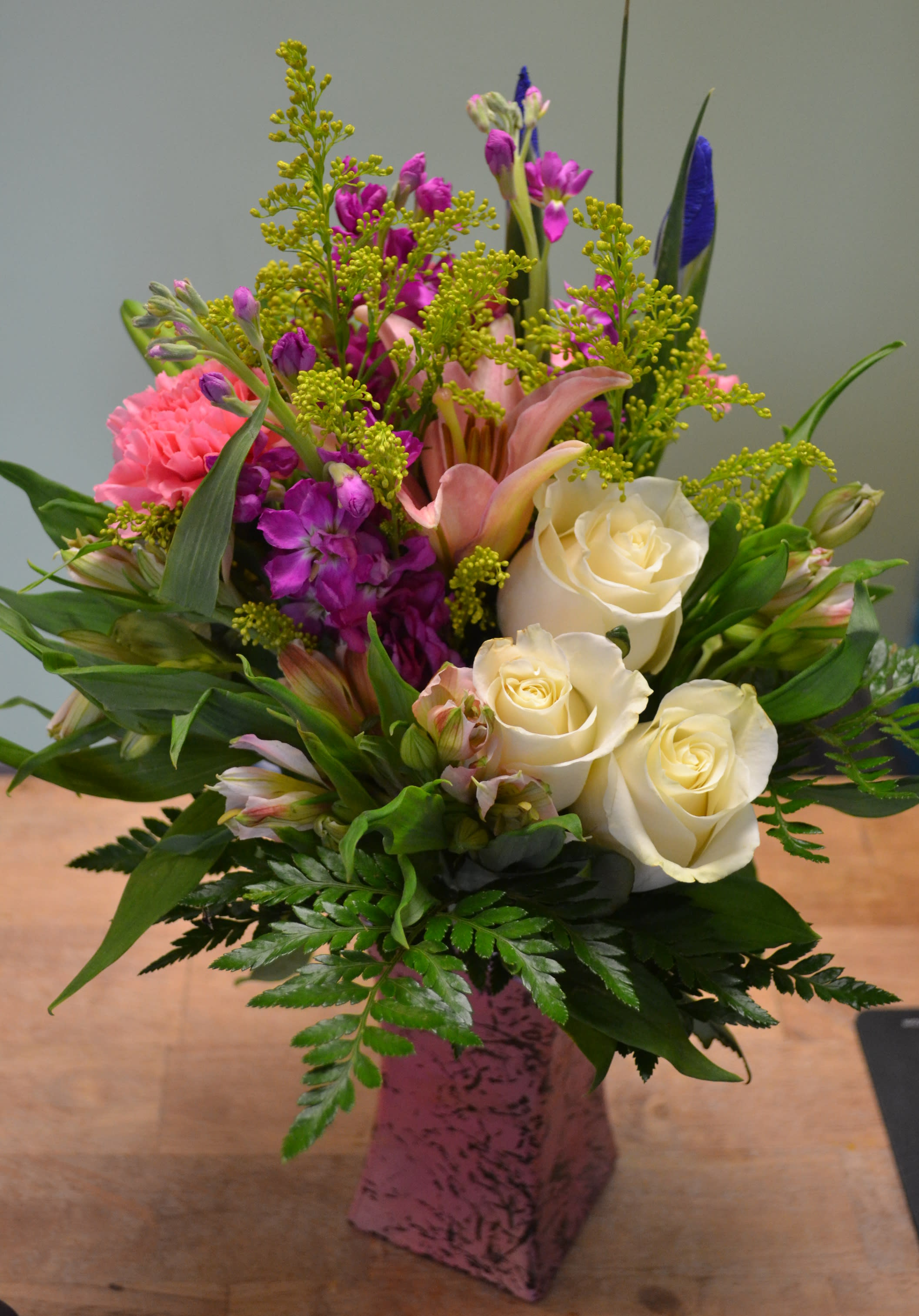 Wonderful Pleasures - This incredible arrangement in a stunning and unusual pink vase includes white roses, Iris, Alstro, Stock, Solidago, Pink Lilies and Carnations and more!