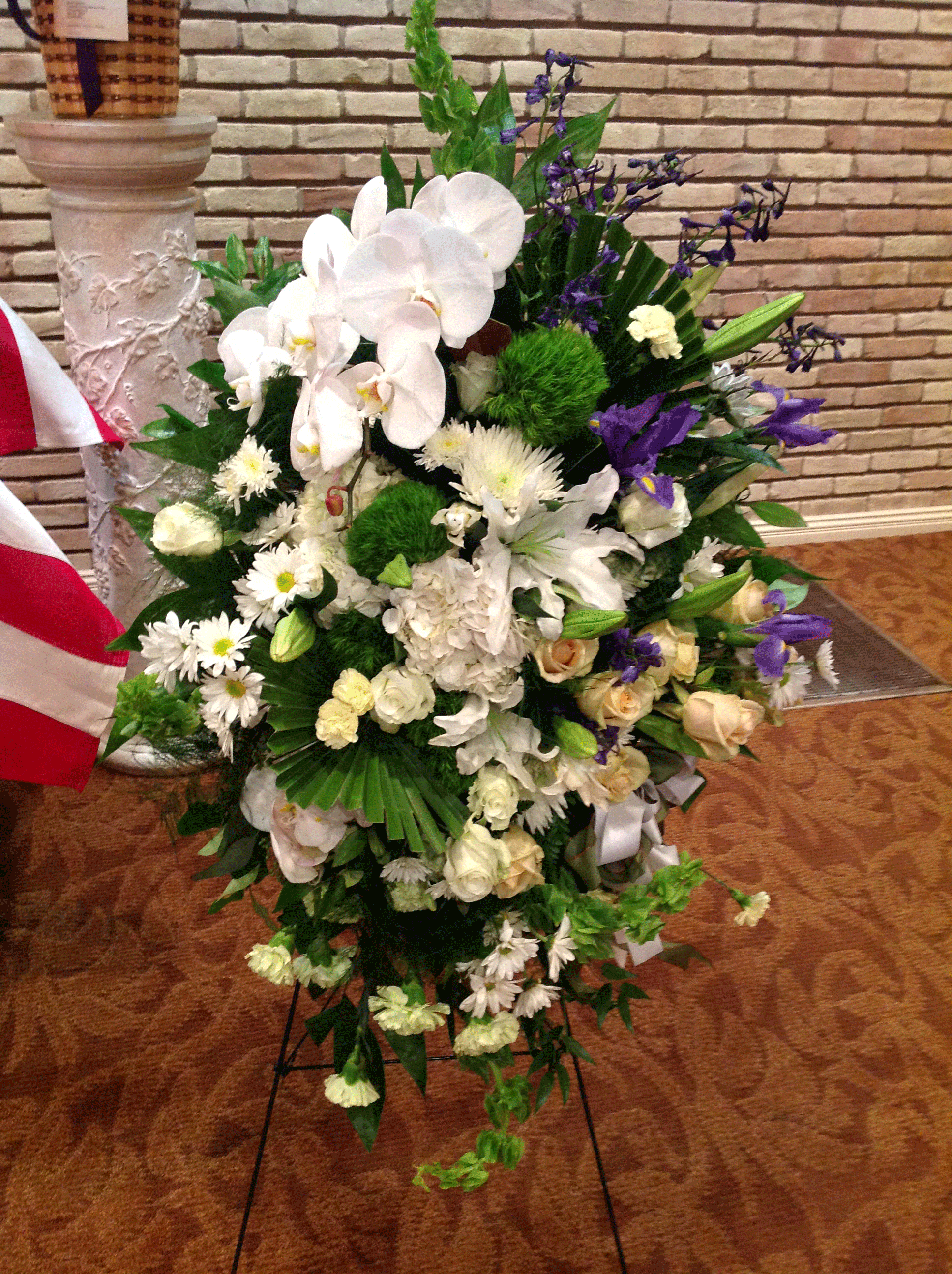 White and Blue Standing Spray - Flowers Included: White Orchids, White Spider Daisies, White Lilies, Roses, Snap dragon flowers, Blue Irises, Green Carnation, White Hydrangea.    Also Included: Pot Vase &amp; Greenery