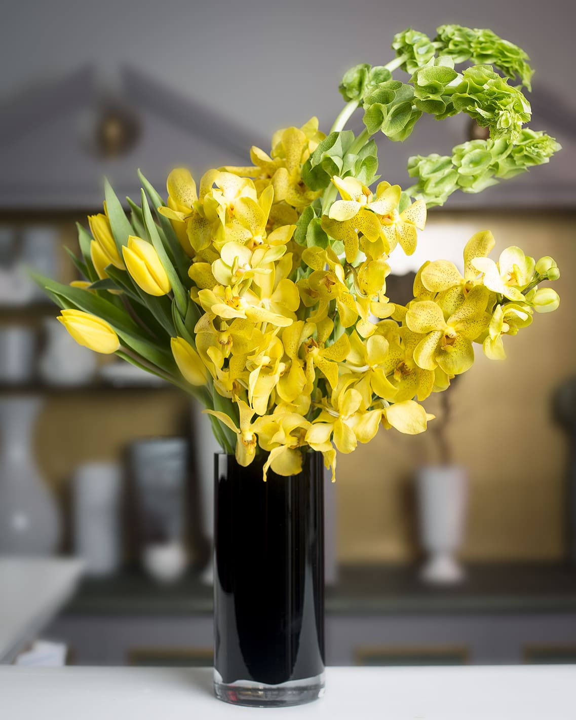 Sunshine - Tulips, bells &amp; mokara orchids in a black glass container.