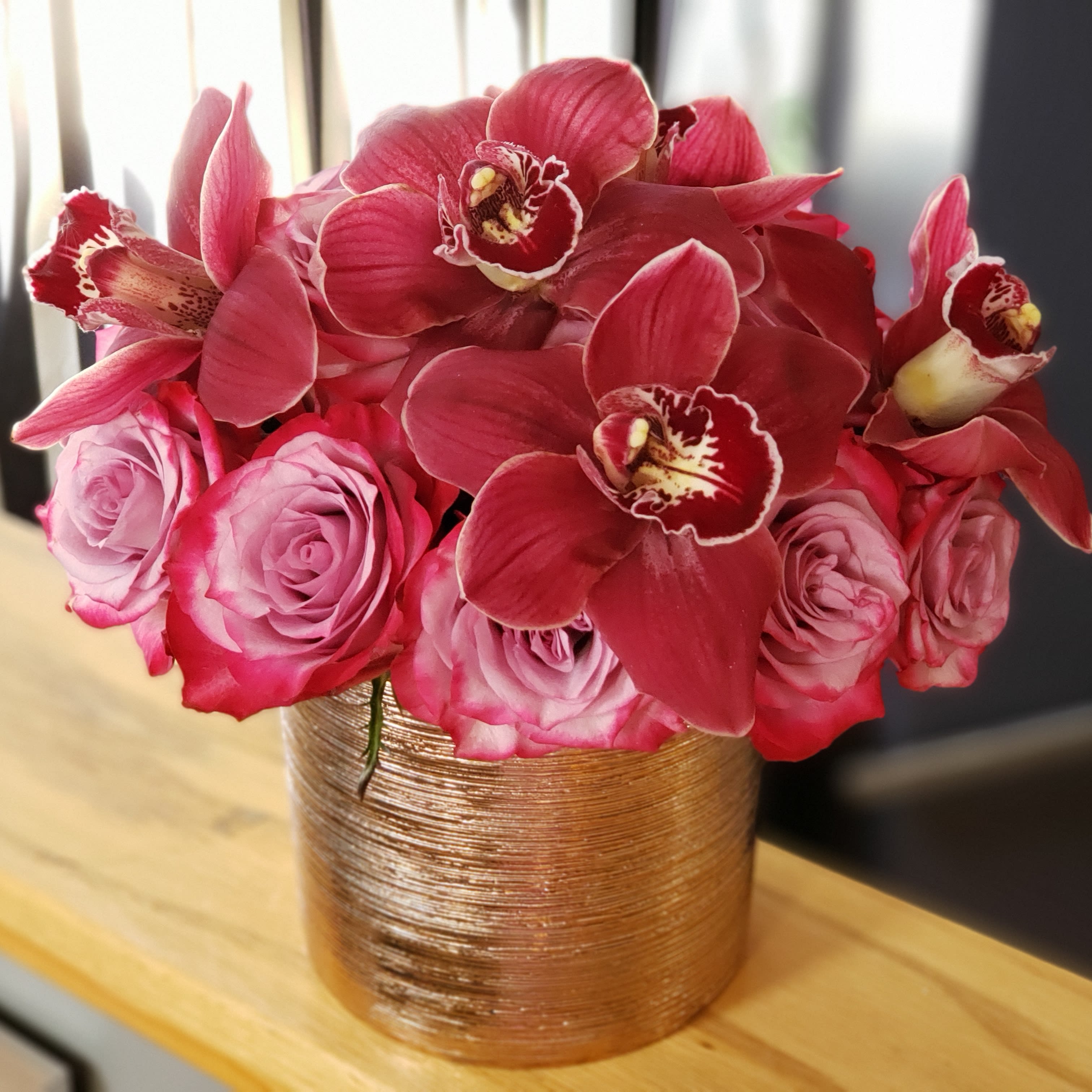 Sandy - 2 dozen roses with cymbidium orchids in a round brushed rose gold container. 
