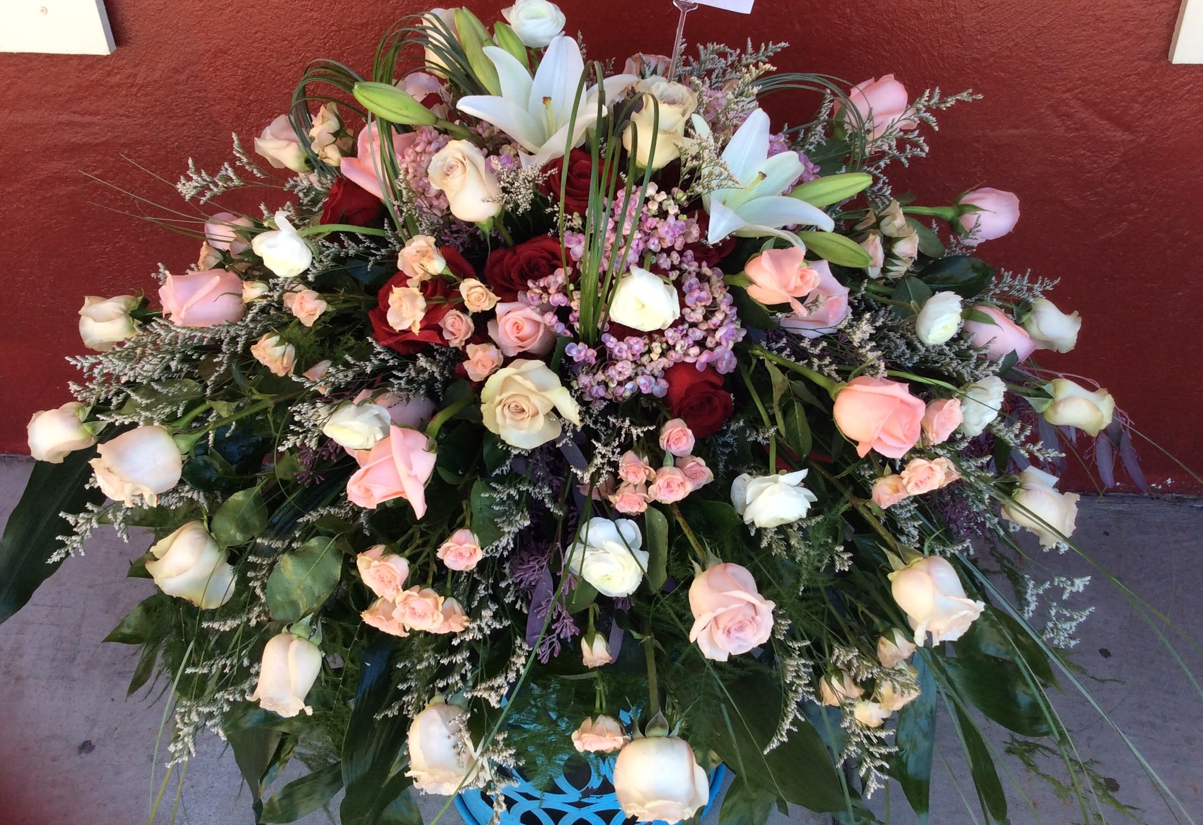 Her Rose Garden - A feminine casket spray with Roses, Hydrangea, Lily, Ranunculus, with accents of seasonal greens &amp; fillers.