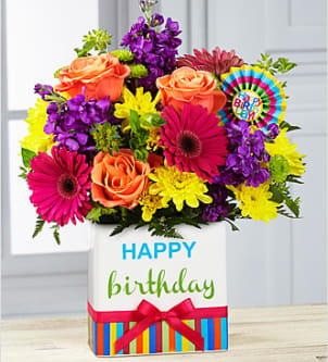 Birthday Brights - The Birthday Brights Bouquet is a true celebration of color and life to surprise and delight your special recipient on their big day! Hot pink gerbera daisies and orange roses take center stage surrounded by purple gilly flowers, yellow chrysanthemums, orange carnations, green button poms, bupleurum, and lush greens to create party perfect birthday display. Presented in a modern rectangular ceramic vase with colorful striping at the bottom, &quot;Happy Birthday&quot; lettering at the top, and a bright pink bow at the center, this unforgettable fresh flower arrangement is then accented with a striped happy birthday pick to create a fun and festive gift