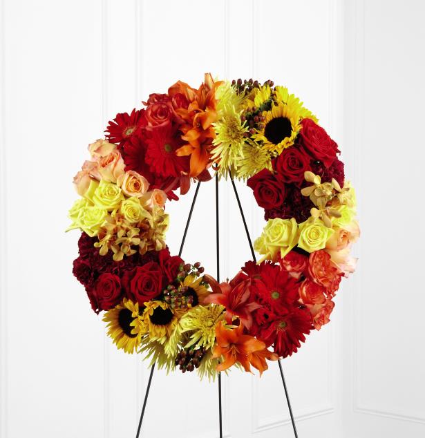 FTD Rurual Beauty Wreath - The FTD Rural Beauty Wreath is a brilliant arrangement that   expresses your grief in the jewel tones of dawn's first light. Peach,   yellow, red, and orange bi-colored roses, burgundy carnations, yellow   spider chrysanthemums, red gerbera daisies, sunflowers, orange Asiatic   lilies, gold mokara orchids, and brown hypericum berries are brought   together to form a wreath that honors a life well-lived. Displayed on a   wire easel.  