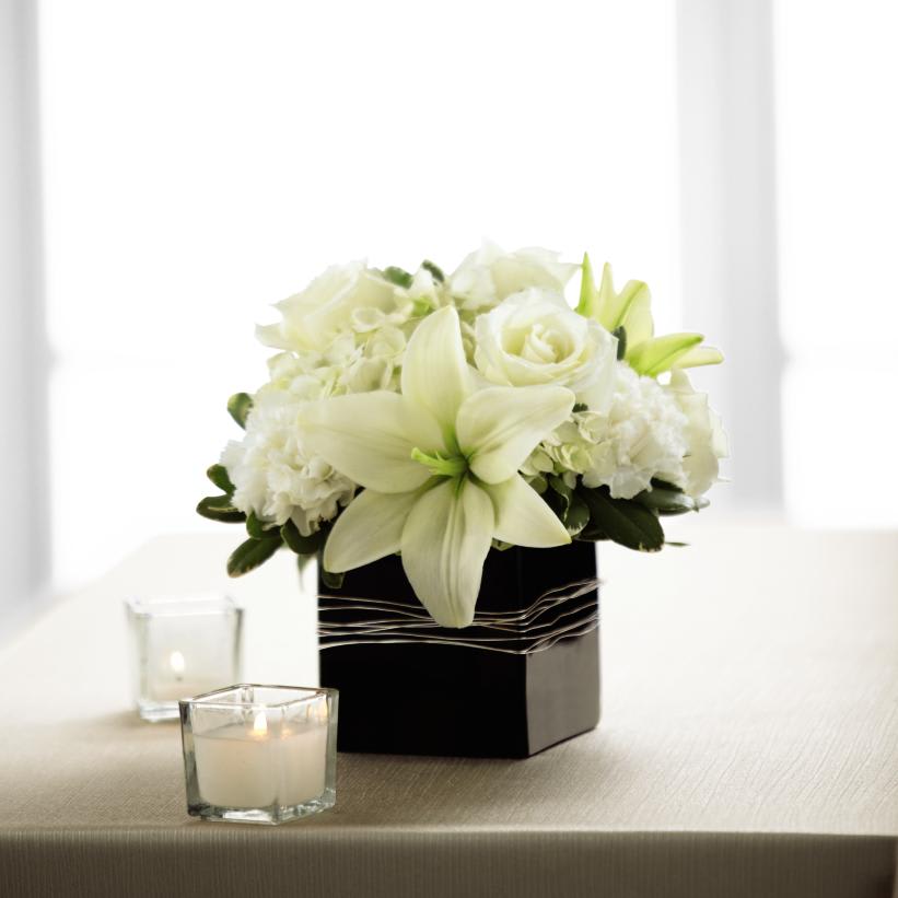  State of Bliss Arrangement - The State of Bliss Arrangement is an ideal centerpiece or accent  piece for the wedding reception. White roses, Asiatic Lilies,  carnations, and hydrangea are offset by lush greens and arranged in a  designer black ceramic cube vase to add to the elegant ambience of this  most momentous day.  Deluxe arrangement includes 9 stems. Approx. 9âH x  9âW. Premium arrangement includes 15 stems. Approx. 10âH x 10âW. BEST  arrangement includes 20 stems. Approx.  11H x 11W. 