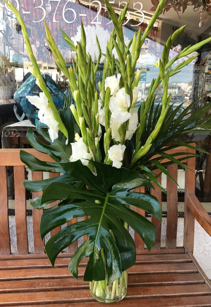 White Gladiolas - Stately white gladiolas fashioned with a striking assortment of tropical leaves. Also available in others colors but we encourage you to call our shop for confirmation.