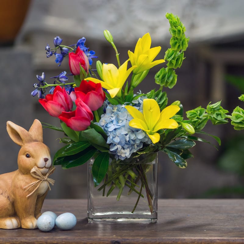 Garden harmony Garden harmony - Red tulips, blue delphinium, yellow lilies, blue hydrangea and green bells of Ireland are beautifully arranged in a clear rectangular vase.