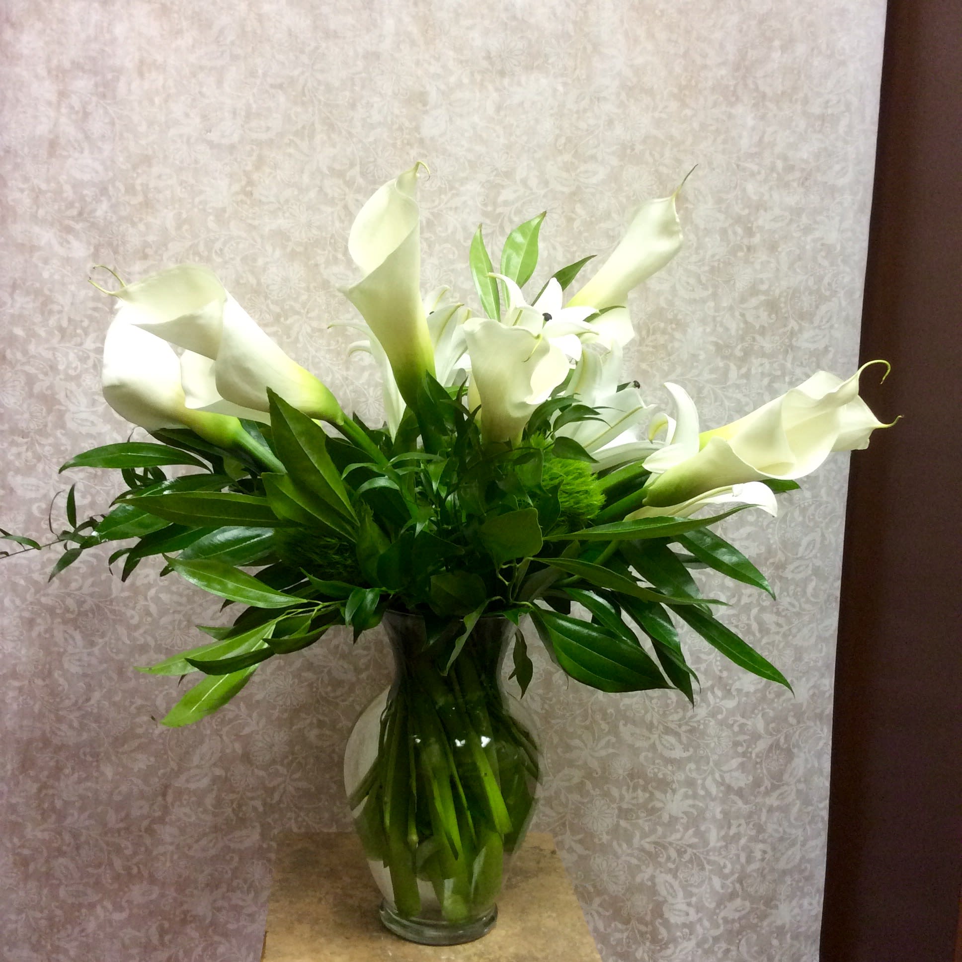 Quiet serenity - Clear glass vase arrangement of white callas and white lilies highlighted with tropical foliage