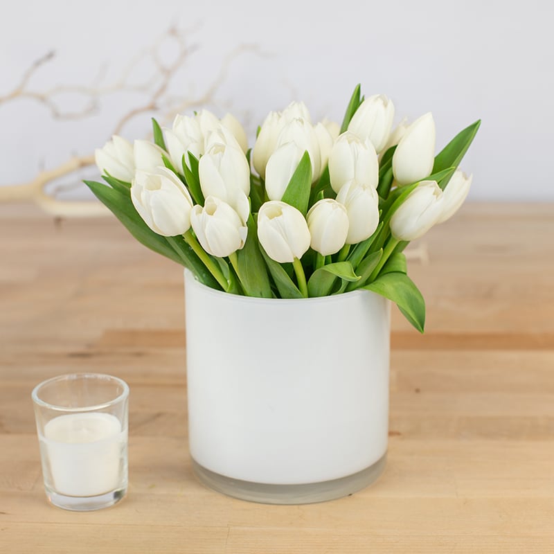 Tulip Arrangement (White) Tulip Arrangement (White) - This fresh, crisp, clean styled arrangement is perfect for any event ranging from a professional business meeting to a friendly hello to a long time friend. Simple and elegant that will surely impress any receiver. Containers come in clear, white, black, and leaf line.