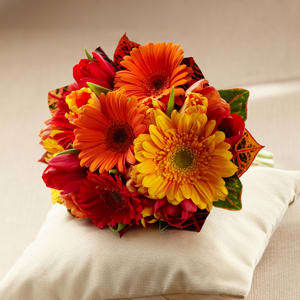 The FTD® Sunglow™ Bouquet -  The FTD® Sunglow™ Bouquet is a blooming wish for happiness and sunlit cheer throughout your lifetime together. Red, orange and bi-colored orange tulips are brought together with red, orange and gold gerbera daisies and colorful croton leaves to create a fantastic eye-catching look. Tied together at the stems with a golden satin ribbon, this bouquet will make the sun shine on your wedding day regardless of the weather. 