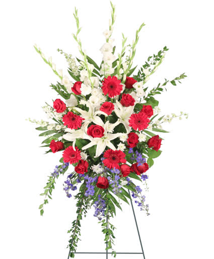 PATRIOTIC SALUTE STANDING SPRAY - Send your beloved patriot off with a standing spray that encompasses the passion they had for their country. The Patriotic Salute standing spray will bring comfort to the hearts of those who are mourning by embodying the patriotism of the hero you lay to rest. This spray features calming white lilies, radiant red Gerbera daisies, and accenting blue delphinium to truly embrace their patriotic spirit.