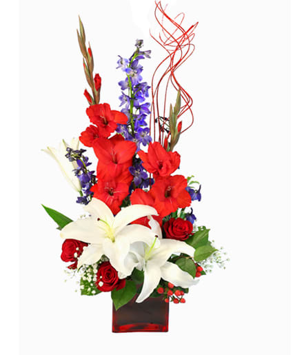 VICTORY FIREWORKS VASE ARRANGEMENT - Celebrate summer time patriotism with an arrangement that stands tall with American pride. The Victory Fireworks arrangement features a red cube vase, vibrant red gladiolus, and brilliant blue delphinium that will bring joy to the heart of any serviceman or veteran. This arrangement is perfect for a centerpiece or just as a patriotic gift with bright white lilies that are like fireworks bursting in the air.